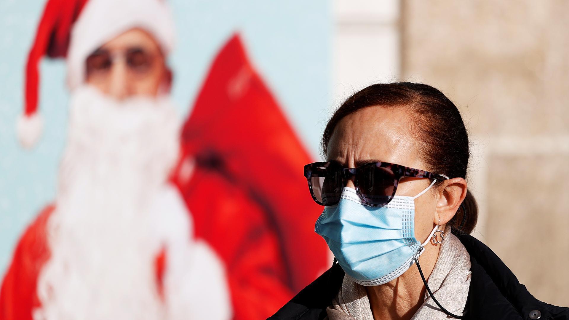 Una mujer pasea por una calle de A Coruña protegida con una mascarilla con un cartel navideño de fondo