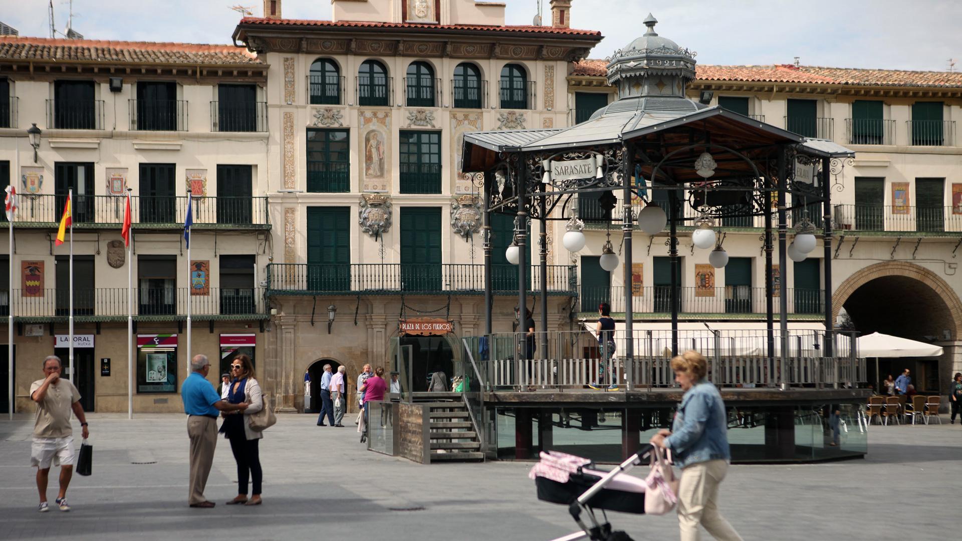 Varias personas pasean junto al quiosco de la plaza de los Fueros, centro neurálgico de Tudela