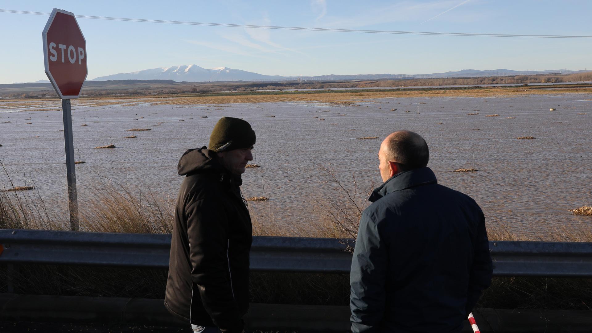 Dos personas miran campos inundados en las inundaciones de diciembre, en la zona de Valtierra