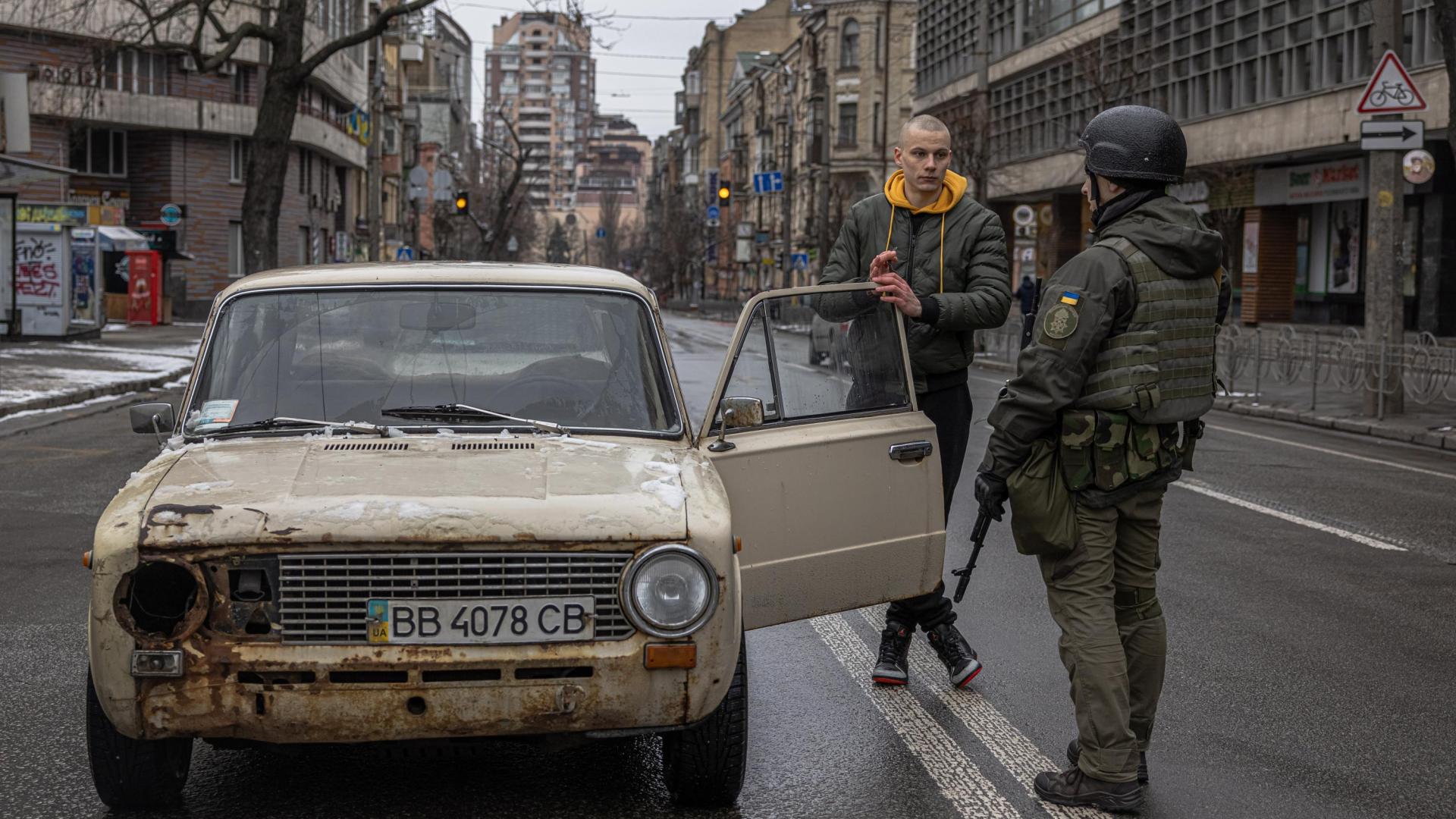 Un miembro de la Guardia Nacional habla con el conductor de un vehículo semidestrozado en el centro de Kiev