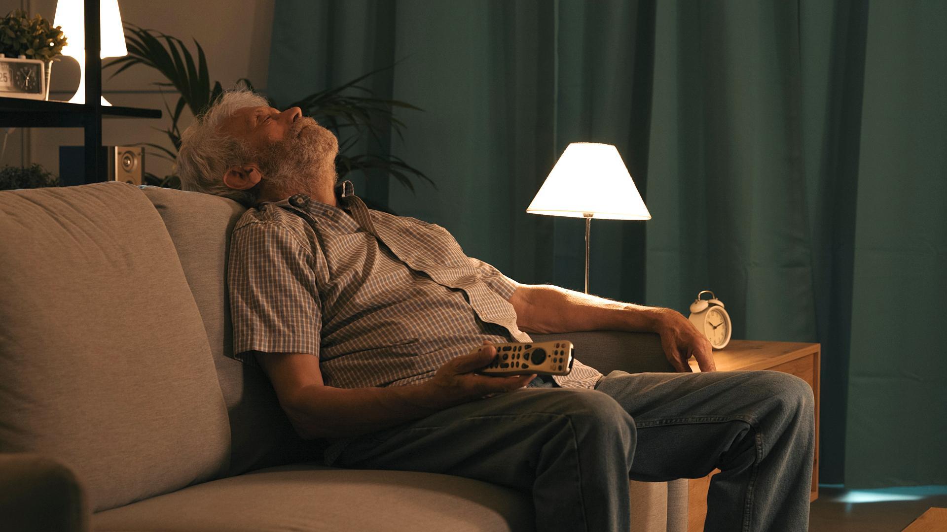 Un hombre mayor se queda dormido en el sofá con el mando de la tele en la mano