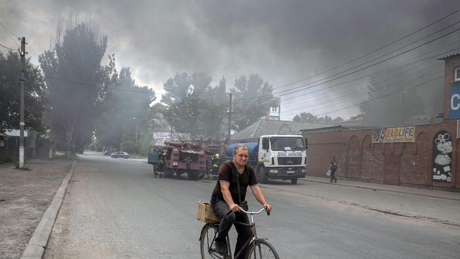 Un hombre circula en bicicleta en la ciudad de Sloviansk, al fondo, la humareda provocada por los ataques rusos