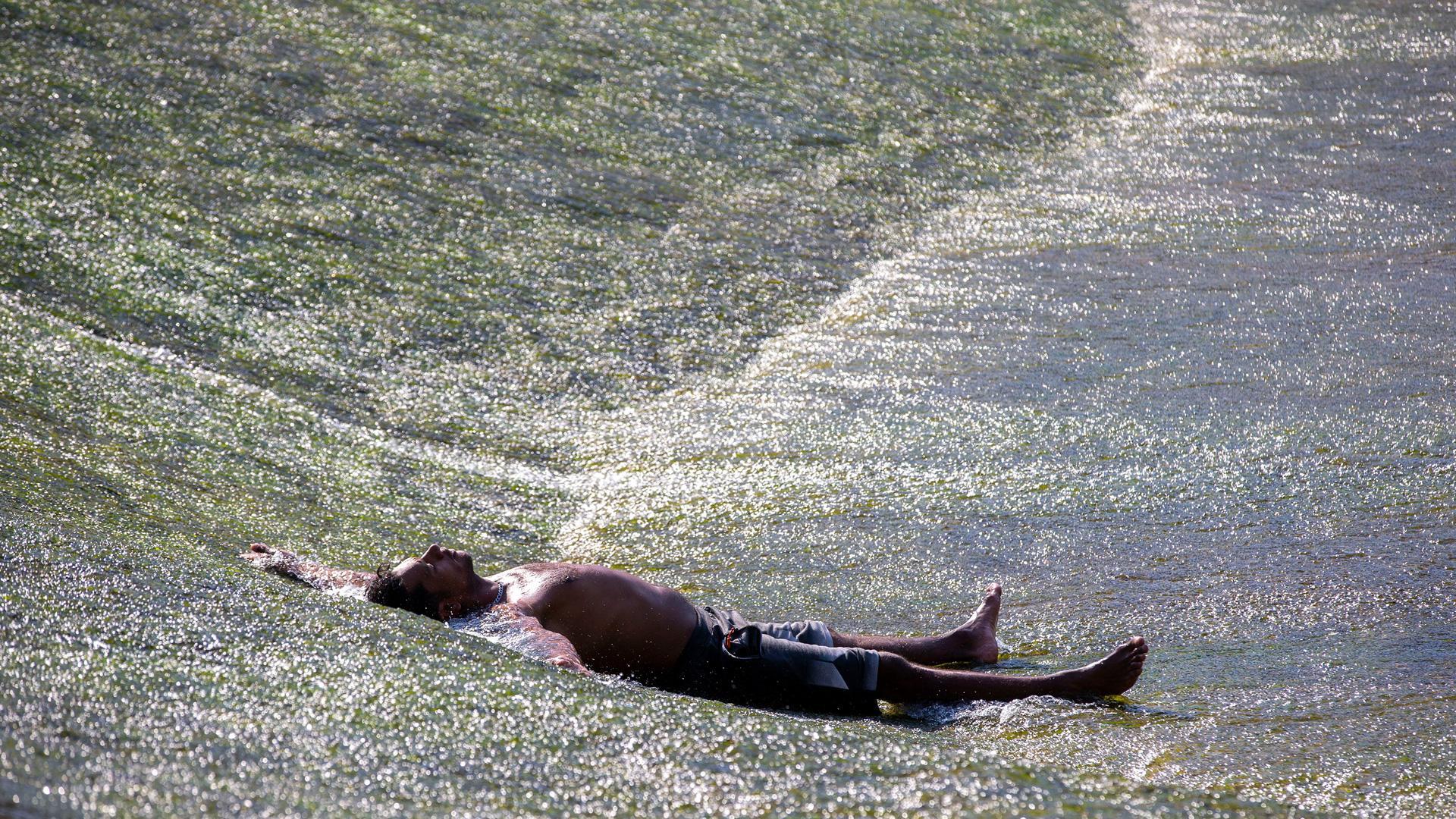 Un hombre se refresca los pasados días de ola calor junto a las pasarelas del río Arga en Pamplona