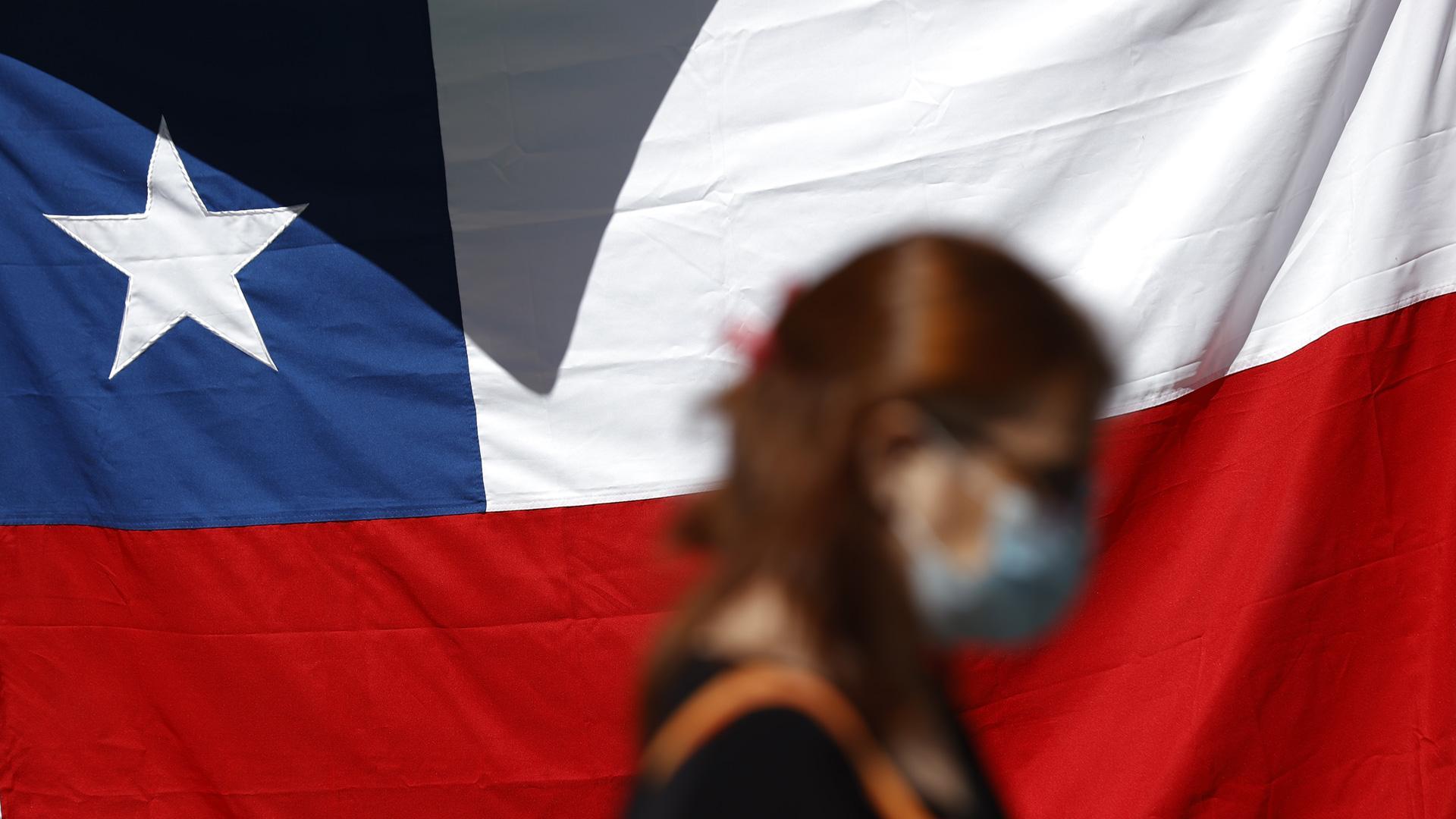 Una mujer camina frente a una bandera de Chile