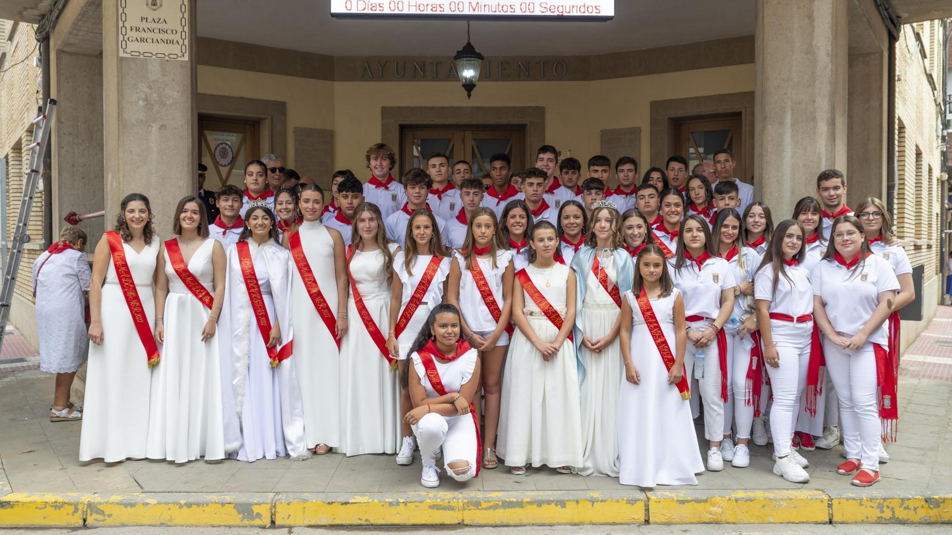 Foto de familia a los pies de la casa consistorial entre quintos, damas y la reina de las fiestas.