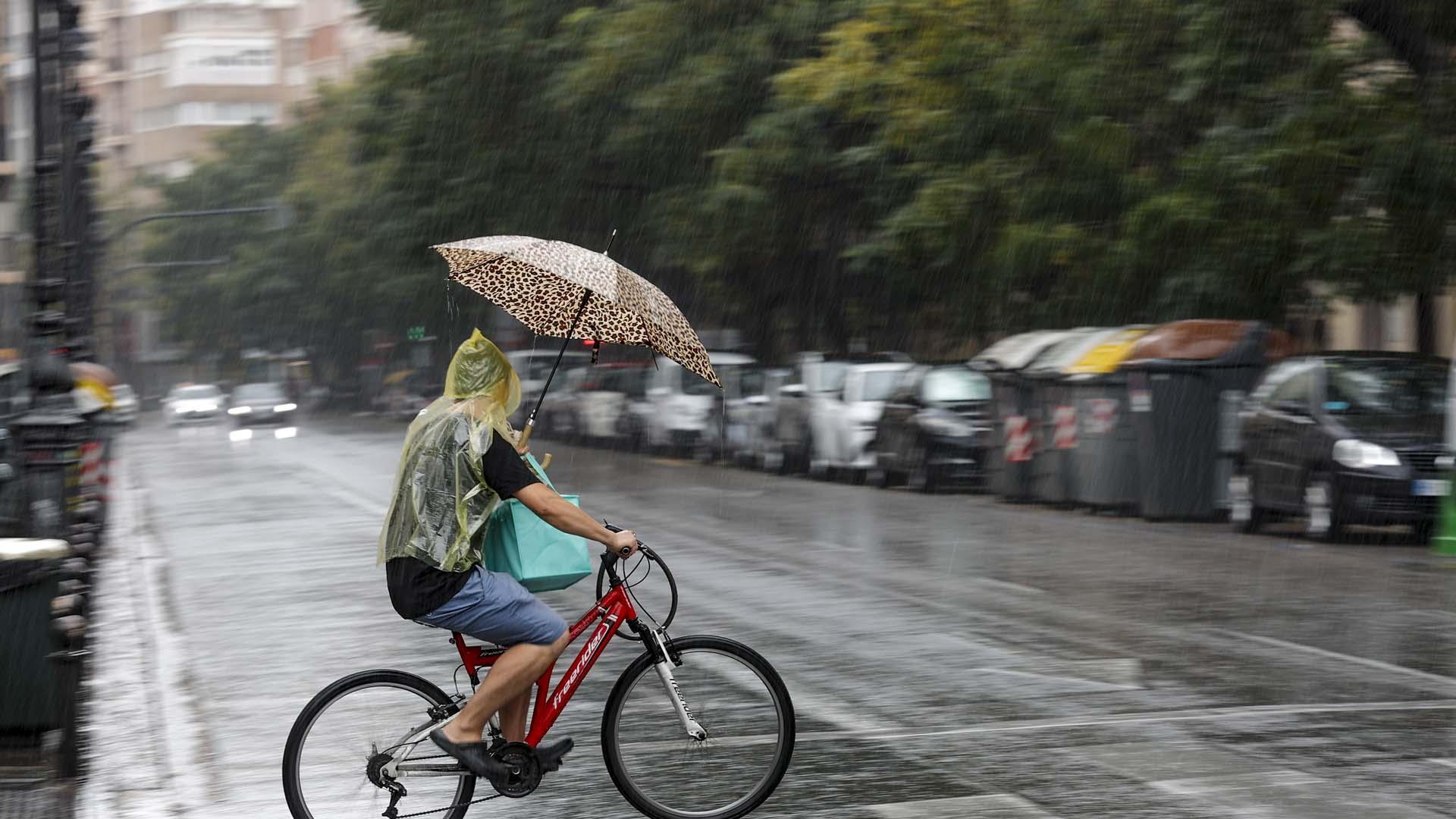 Un hombre circula en bicicleta bajo la lluvia en Valencia