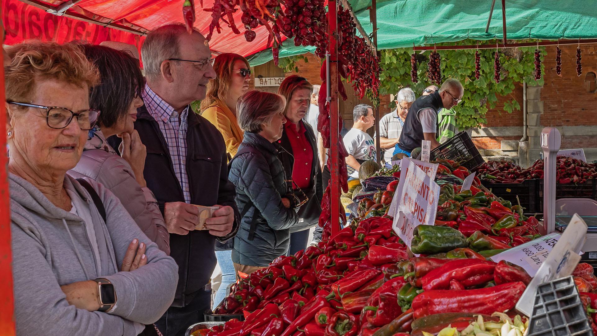 Varias personas esperan en un puesto de pimientos de Puente la Reina a ser atendidas mientras  observan y eligen el tipo de pimiento que van a adquirir