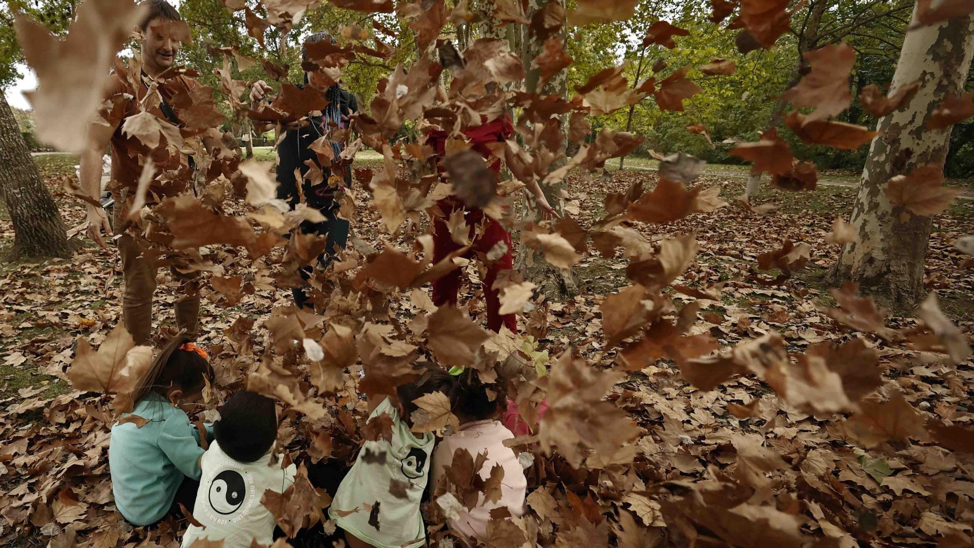 Un grupo de padres juegan con sus hijos lanzándoles las hojas secas caídas de los arboles en un parque de Pamplona