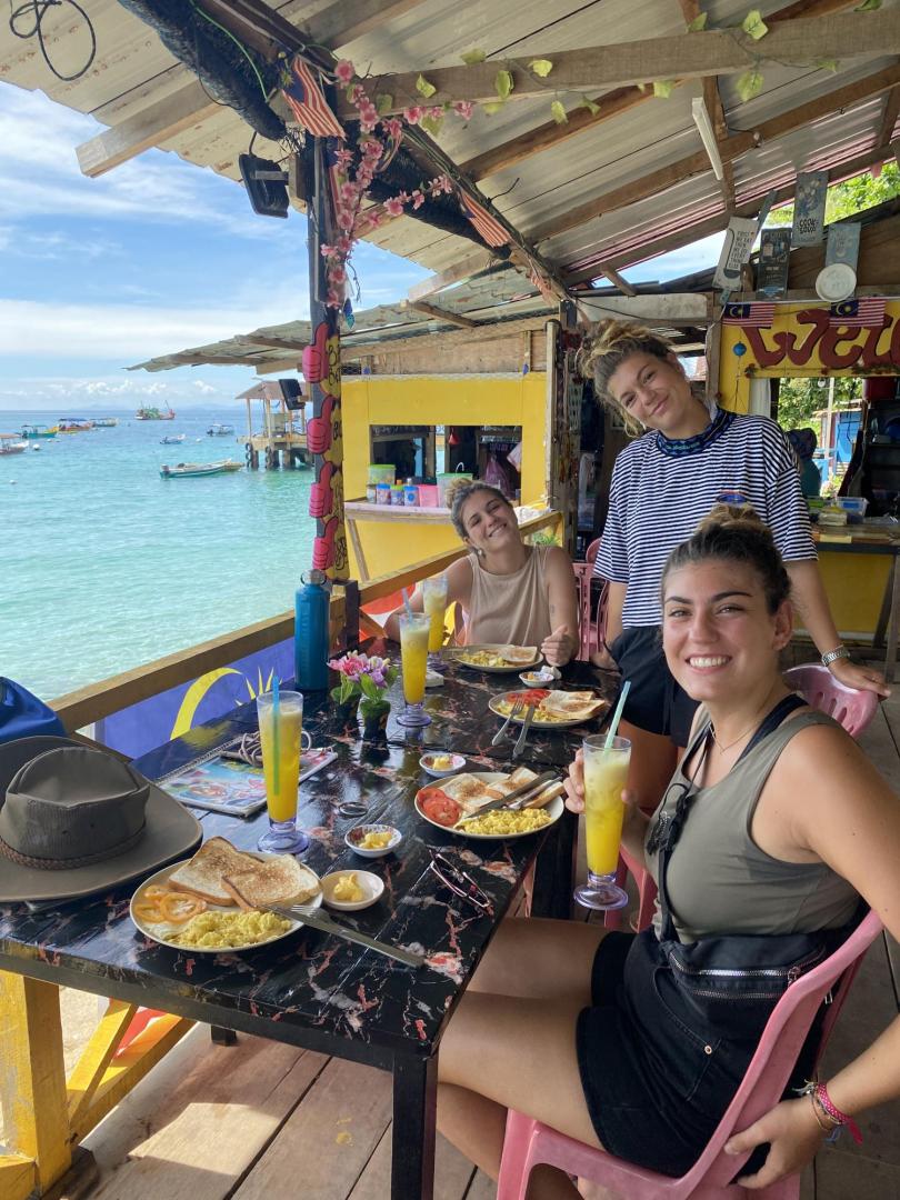 Paula Barba (de pie), junto a sus hermanas Patricia y Nora (al fondo), comiendo en Perhentian Island (Malasia).