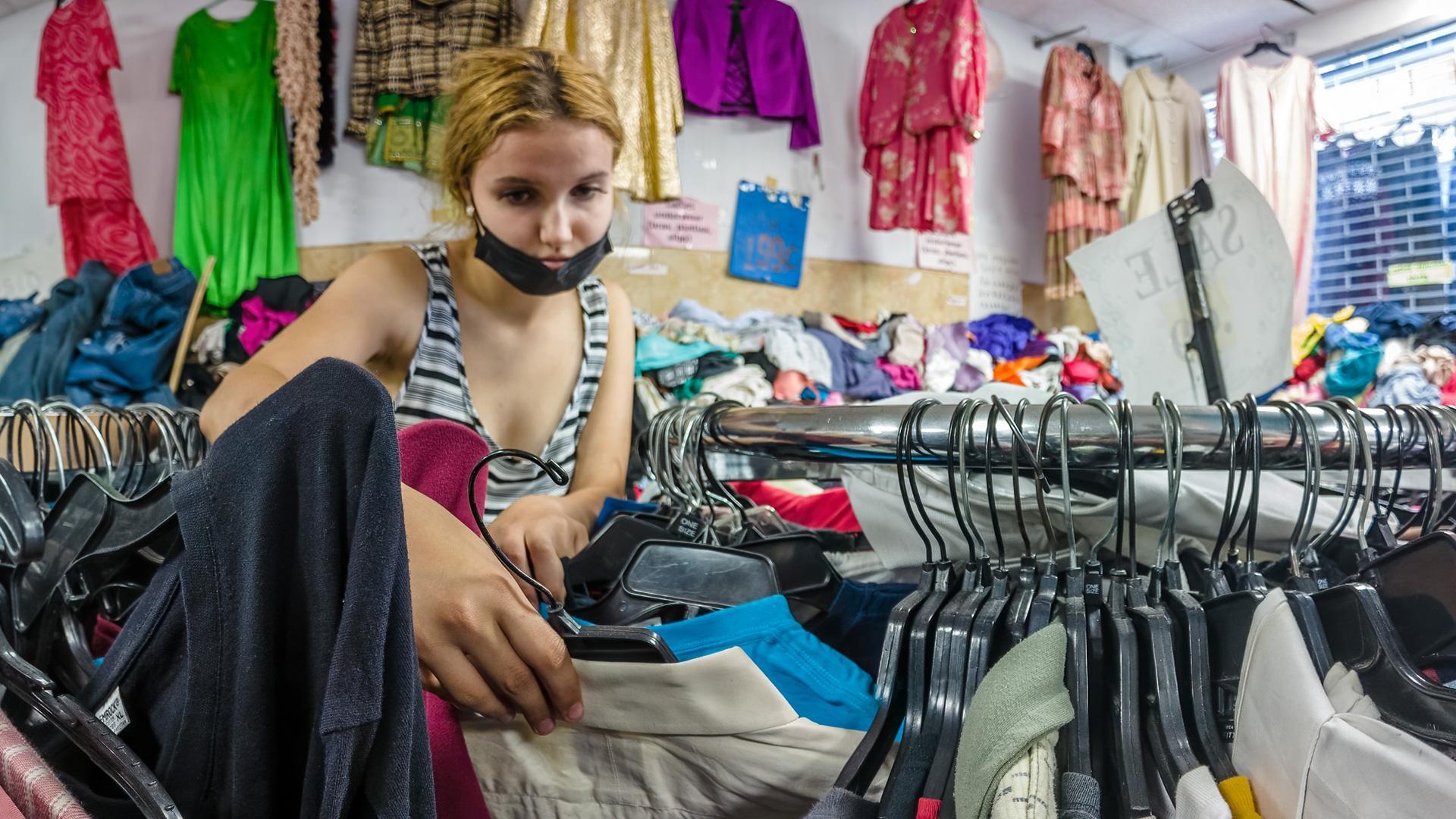 Una joven busca una prenda en una tienda de ropa de segunda mano
