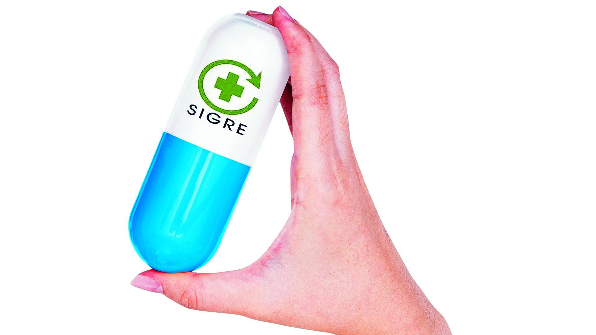 Una mano sujeta una cápsula con forma de medicamento con el logotipo del Sigre