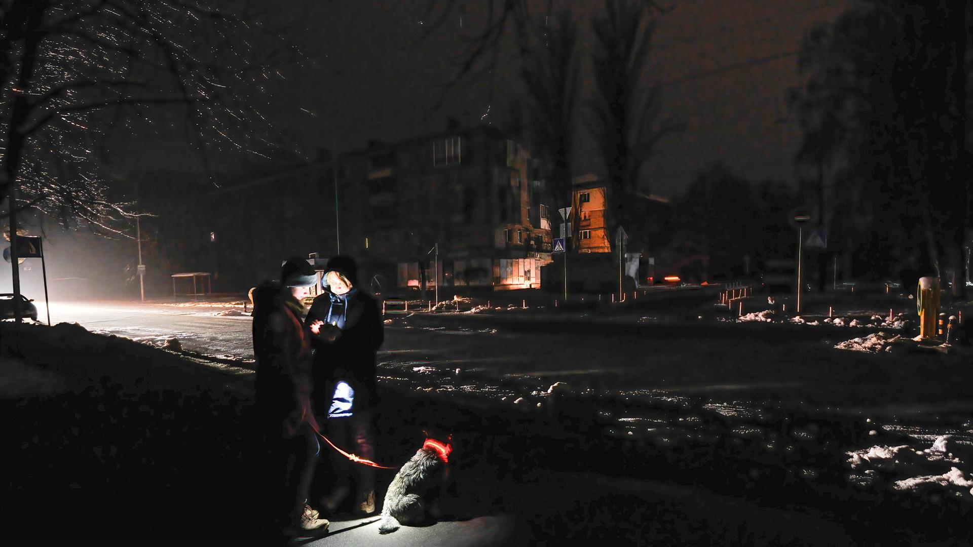 Dos personas se alumbran con un teléfono móvil en una calle oscura de Kiev, donde la mitad de la ciudad sigue sin electricidad y dos tercios de los hogares no tienen calefacción