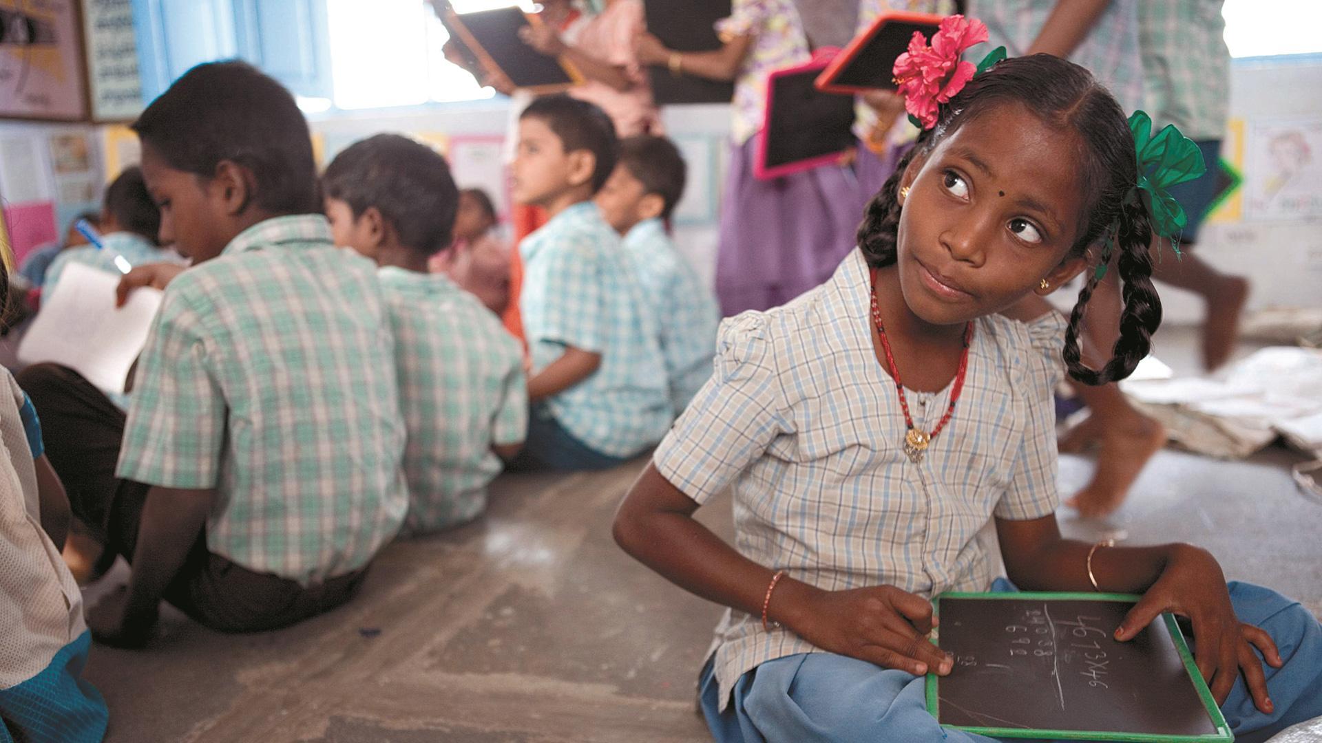 Una niña india escribe unos números en su pizarra, en la escuela