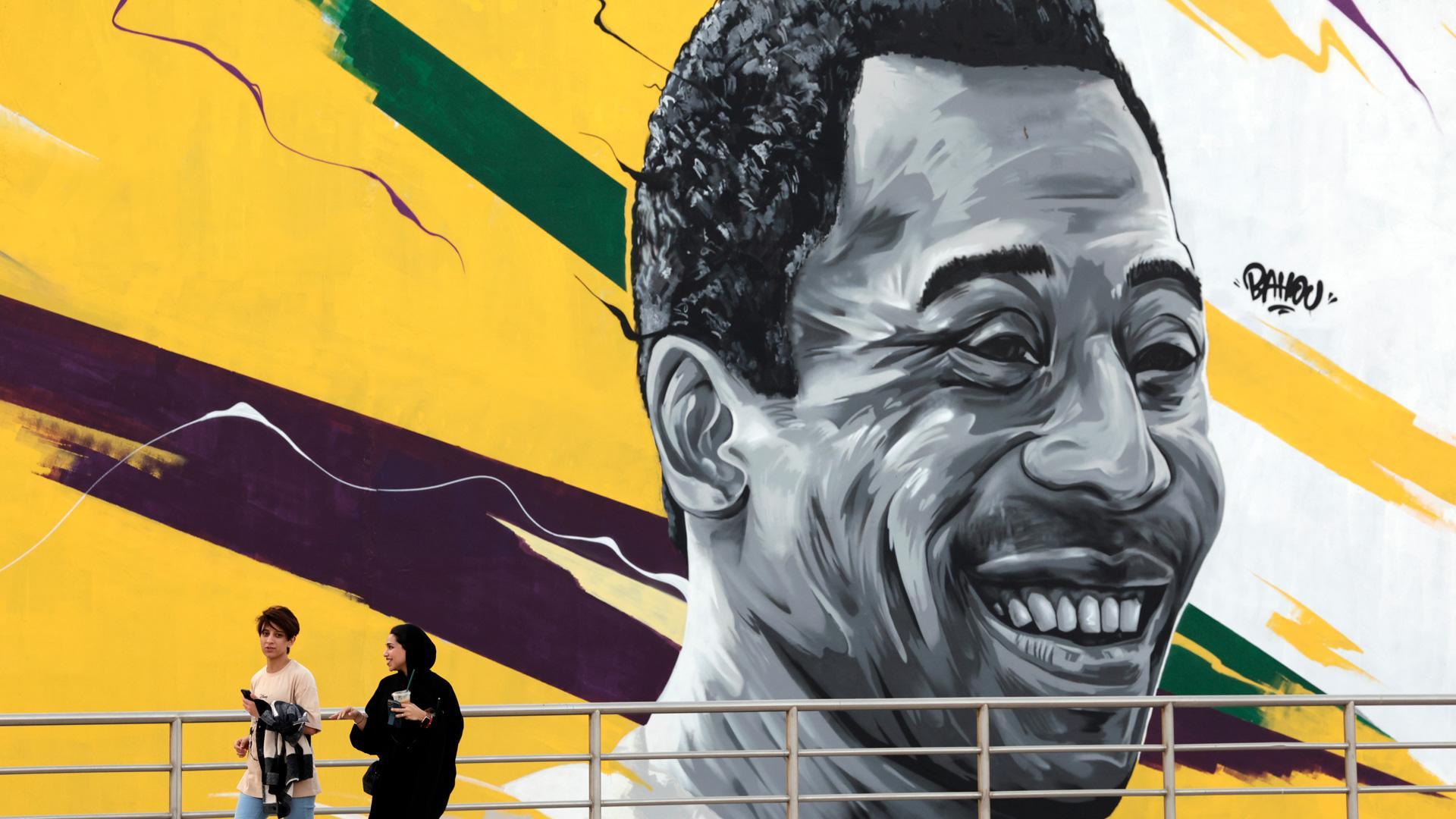 Unas mujeres pasan delante de un mural que representa al exjugador brasileño Edson Arantes do Nascimento, "Pelé" enfrente del estadio Al Khalifa de Doha, Catar