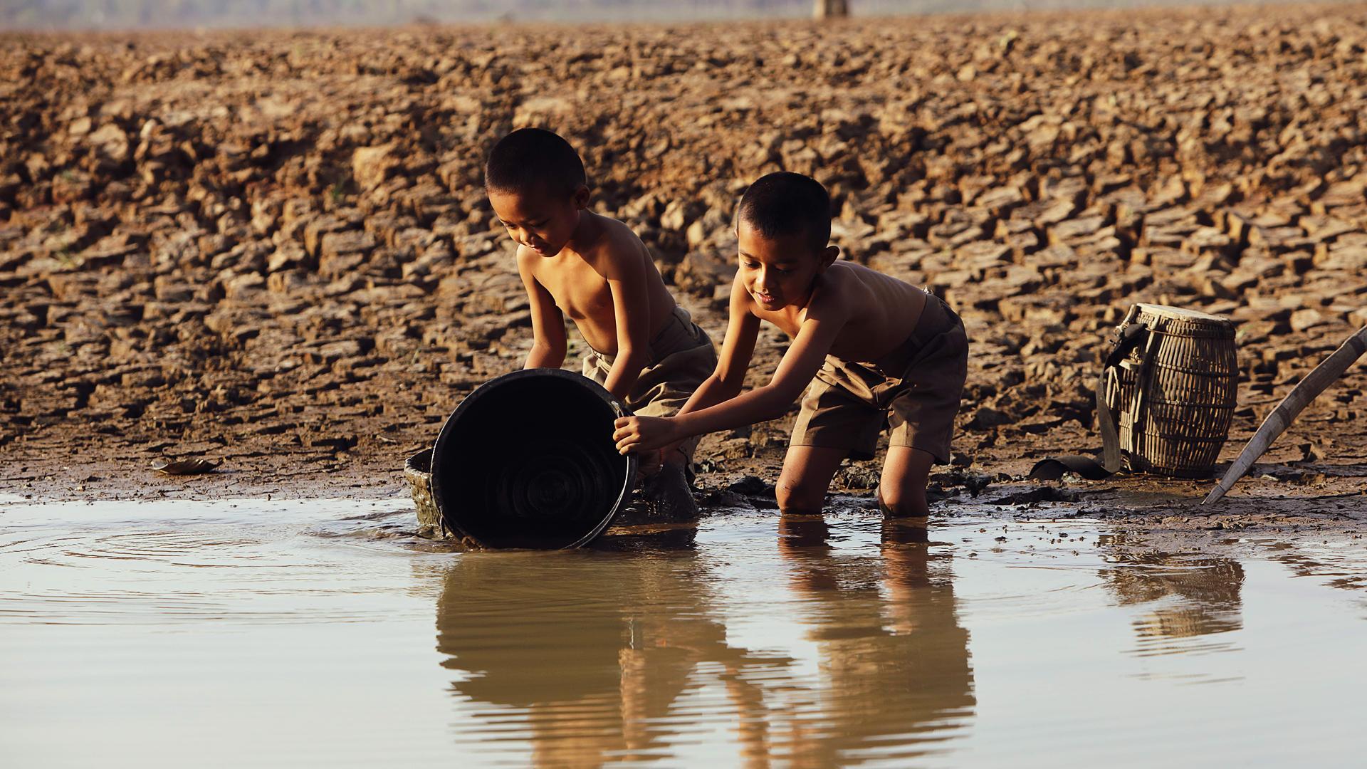 Dos niños juegan con un cubo en la orilla de un río.