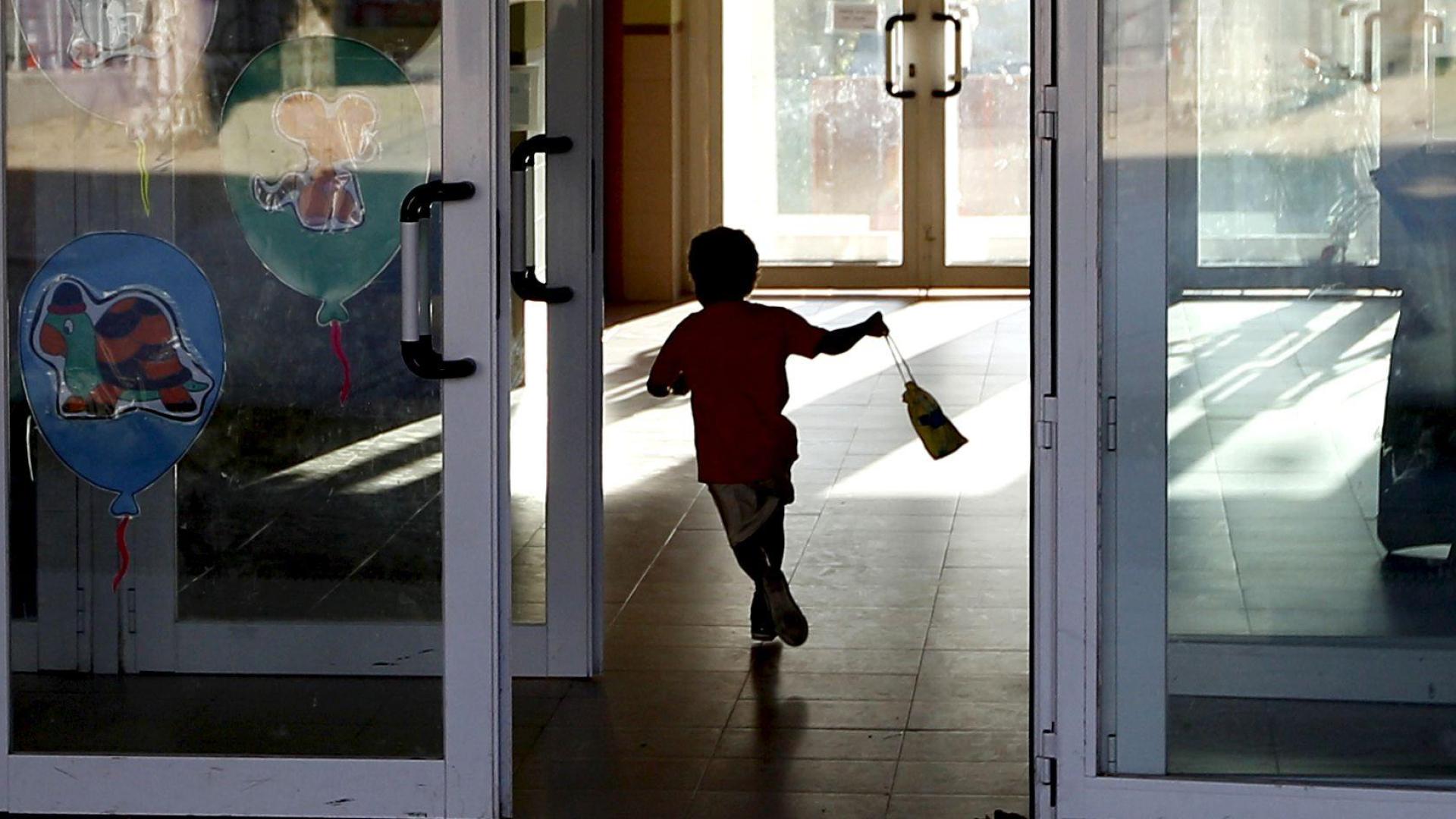 Un niño atraviesa la puerta del colegio con la bolsa del almuerzo en la mano
