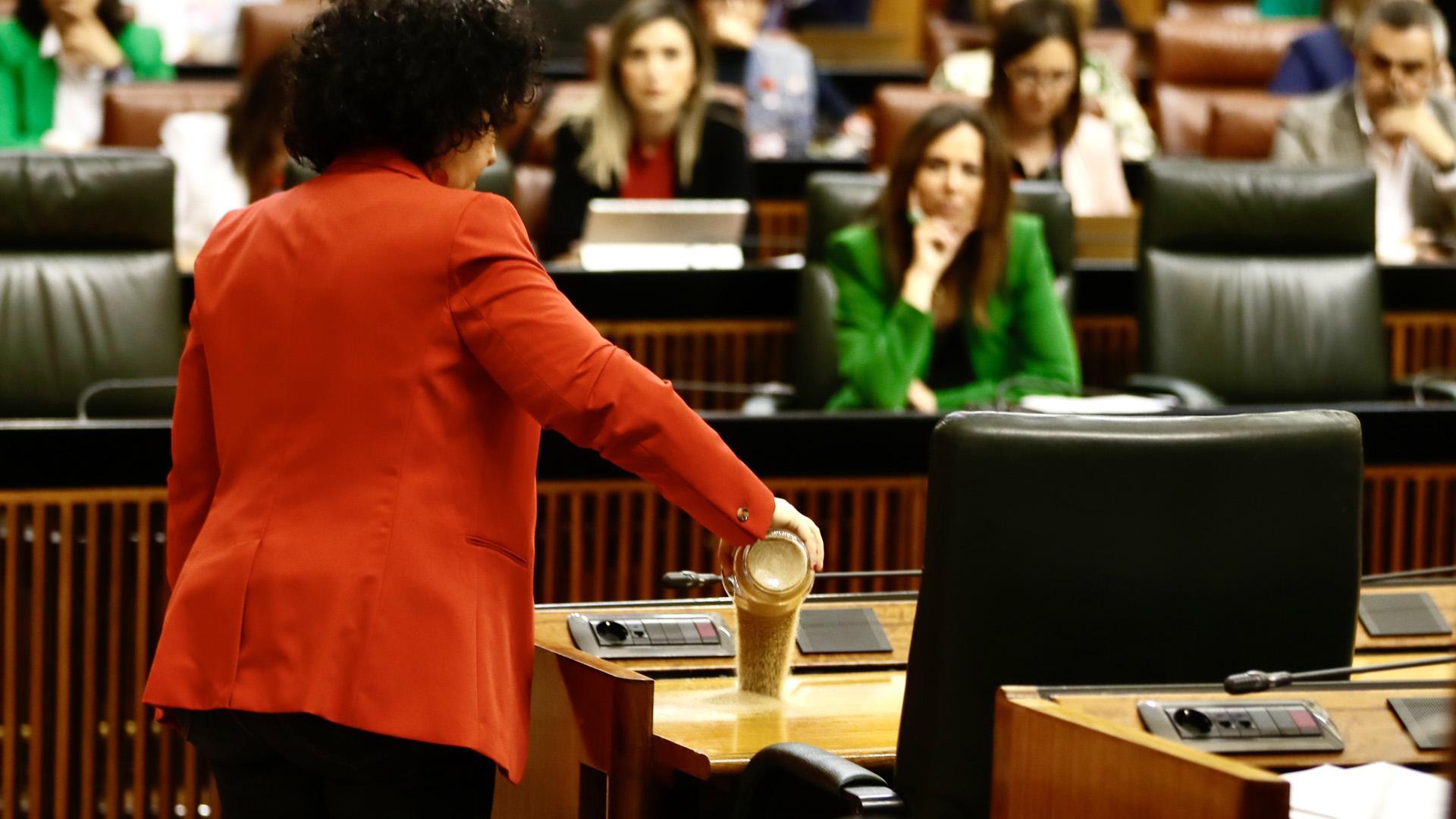 La diputada del Grupo Mixto Maribel Mora derrama arena en el escaño del presidente de la Junta, Juanma Moreno, durante el pleno del Parlamento andaluz donde se debate una proposición de ley del PP y Vox para reordenar los regadíos de la Corona Norte de Doñana