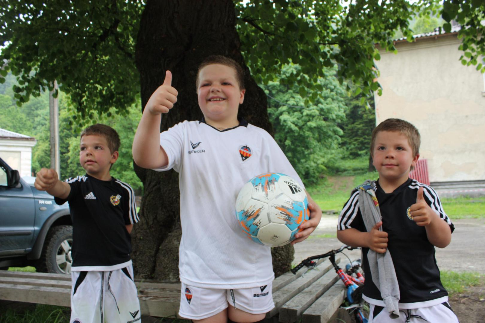 Tres niños refugiados sonríen después de recibir material deportivo llevado desde Pamplona por la fundación Enfermeras de Navarra