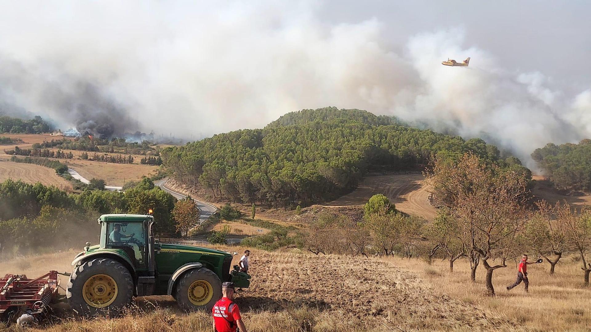 Desde lo alto del pueblo varias personas observan con preocupación las llamas acercarse y a los medios aéreos intentando sofocar el fuego