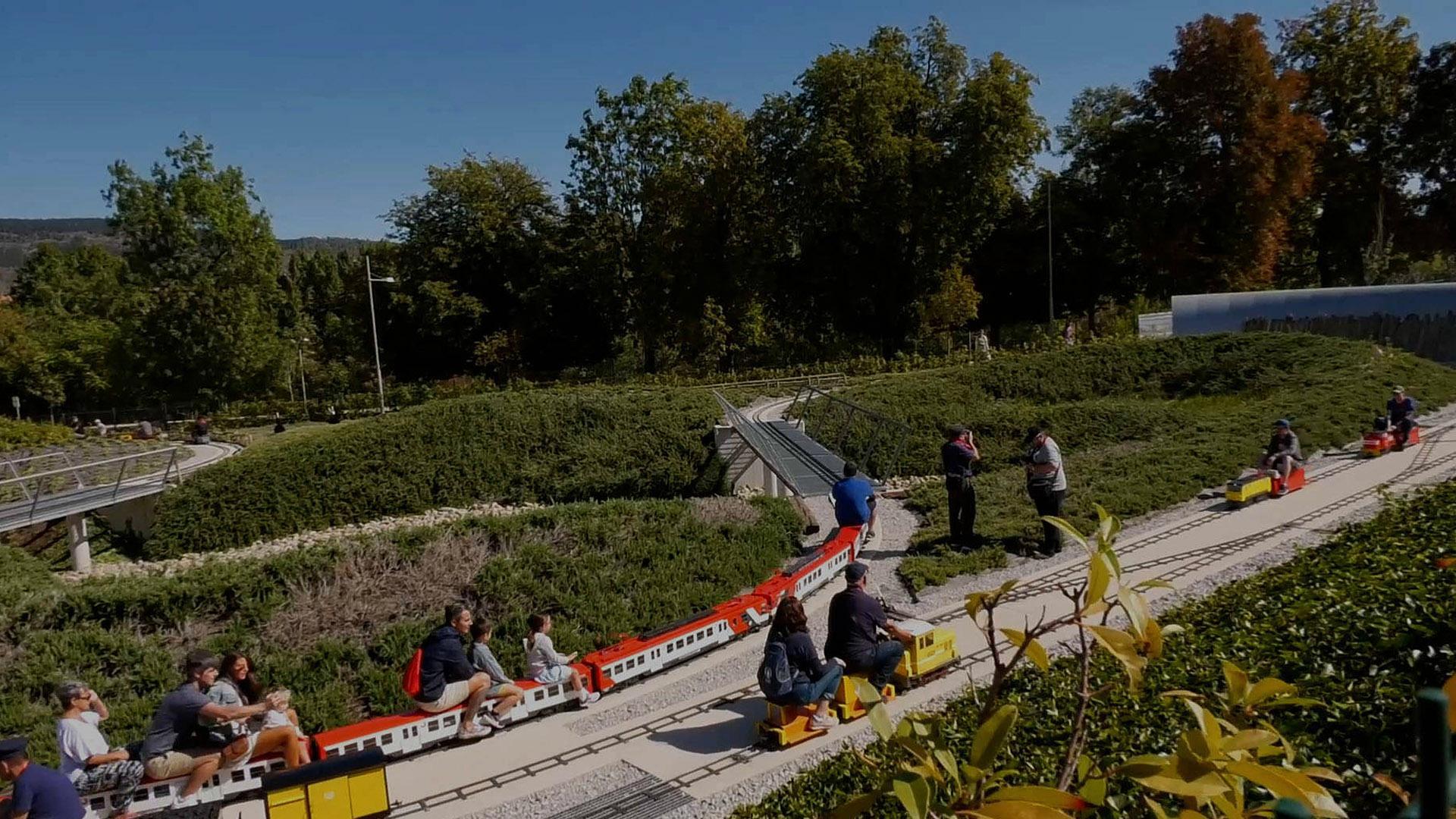 Una imagen en la que se puede ver a varias personas, incluidos niños, disfrutando de los trenes a escala en el parque
