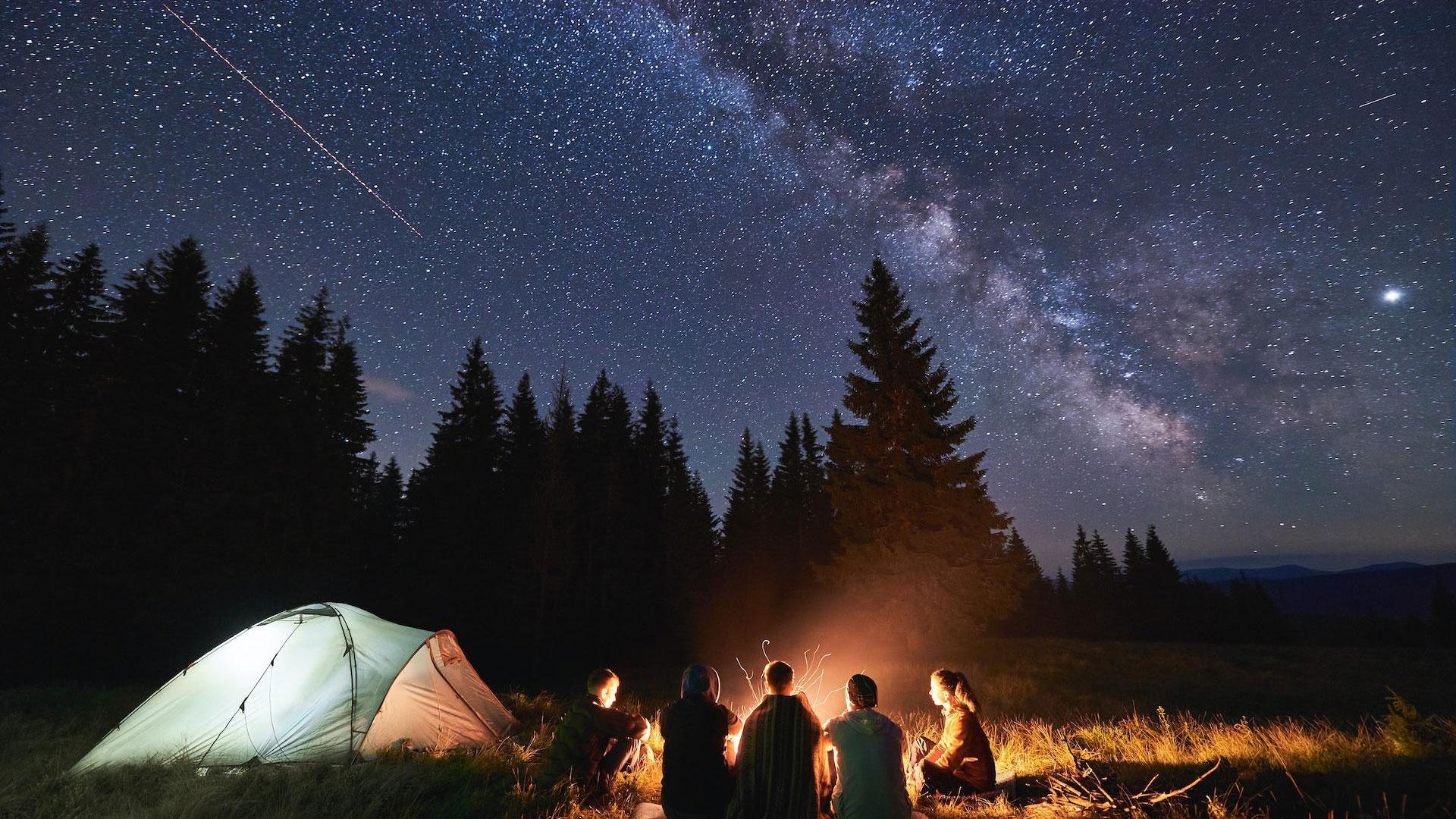 Unos jóvenes contemplan el cielo estrellado durante una acampada