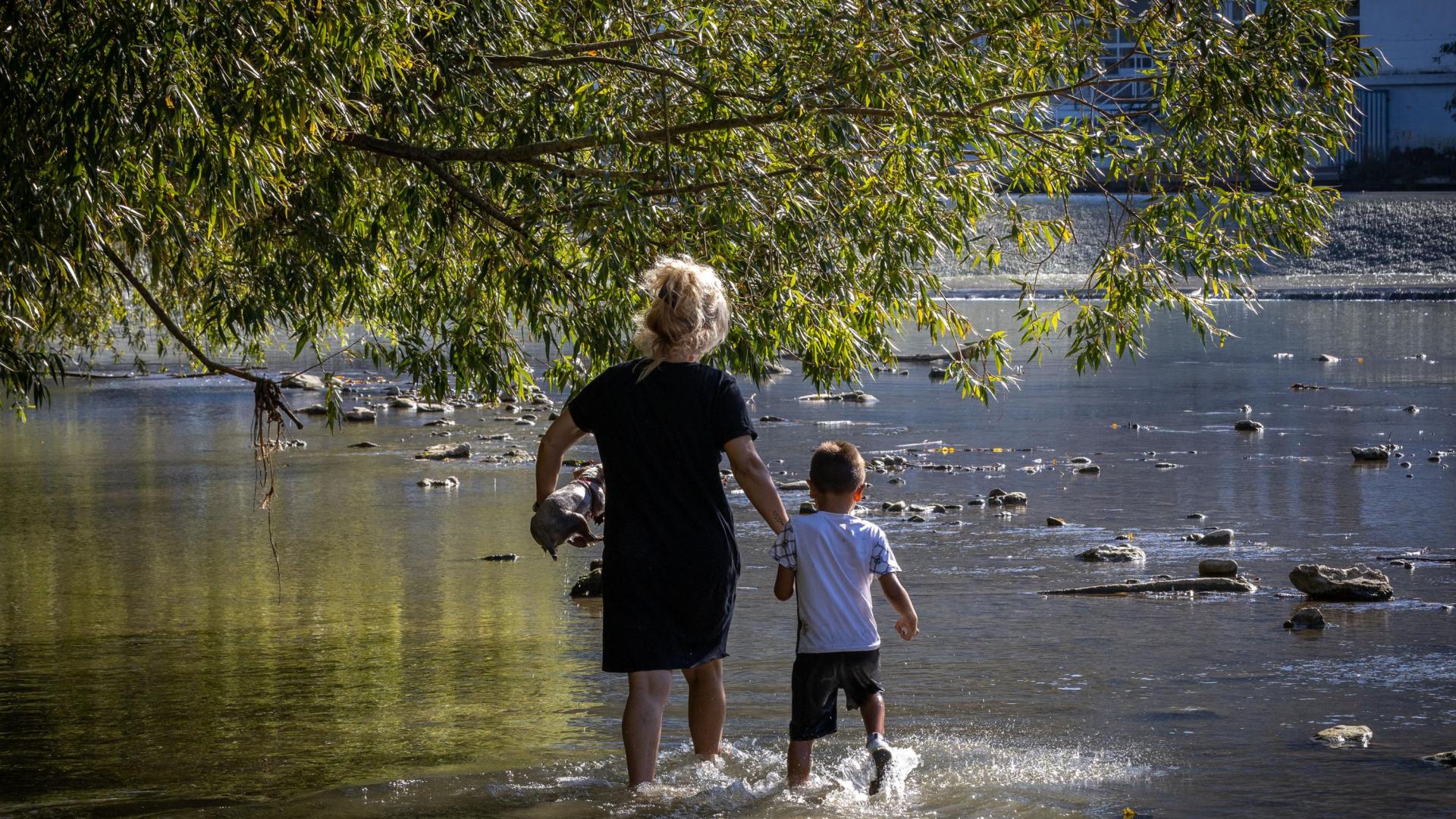 Una mujer y un niño se refrescan en las aguas del Arga, junto a las pasarelas de la Magdalena.