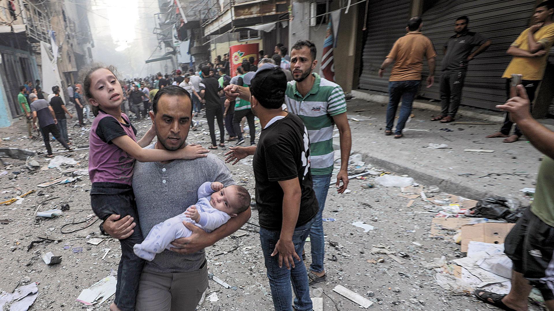 Un hombre sostiene a una niña y a un bebé mientras huye del lugar de un ataque con cohetes israelíes en el campo de refugiados de Al-Shati, en el oeste de la ciudad de Gaza