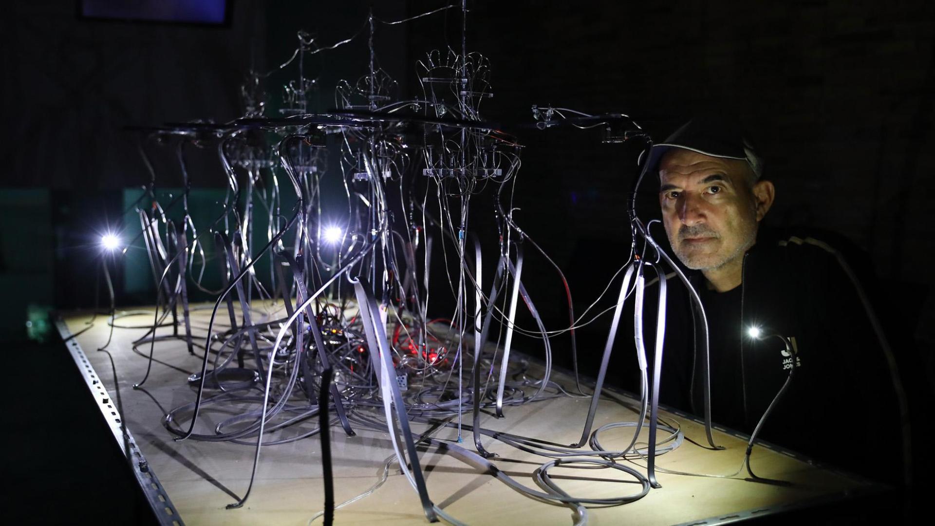 Patxi Araujo posa en la oscuridad junto a Analemma(Mesa para 10) compuesta por diez robots que emiten luz y movimiento