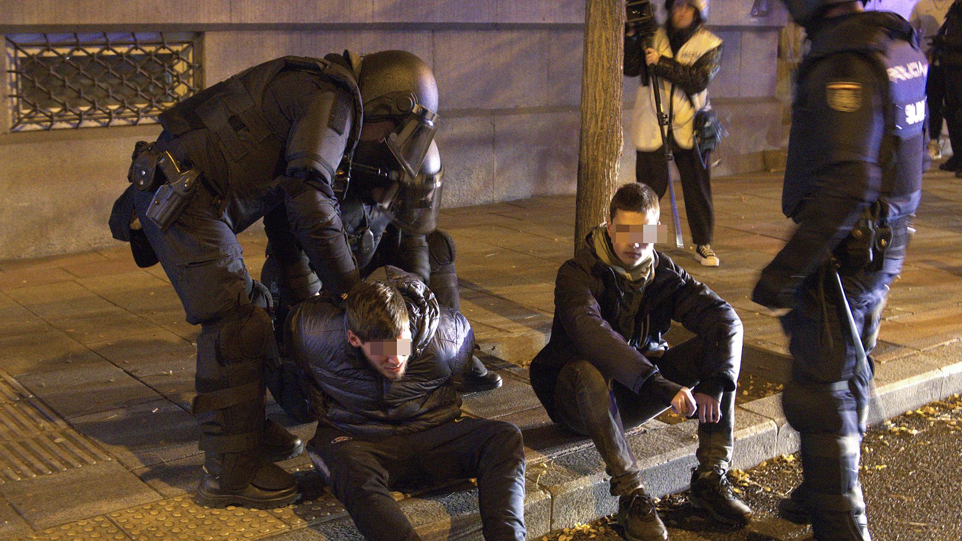 Agentes de la Policía Nacional esposan a dos de los detenidos tras los incidentes ante la sede del PSOE en Ferraz
