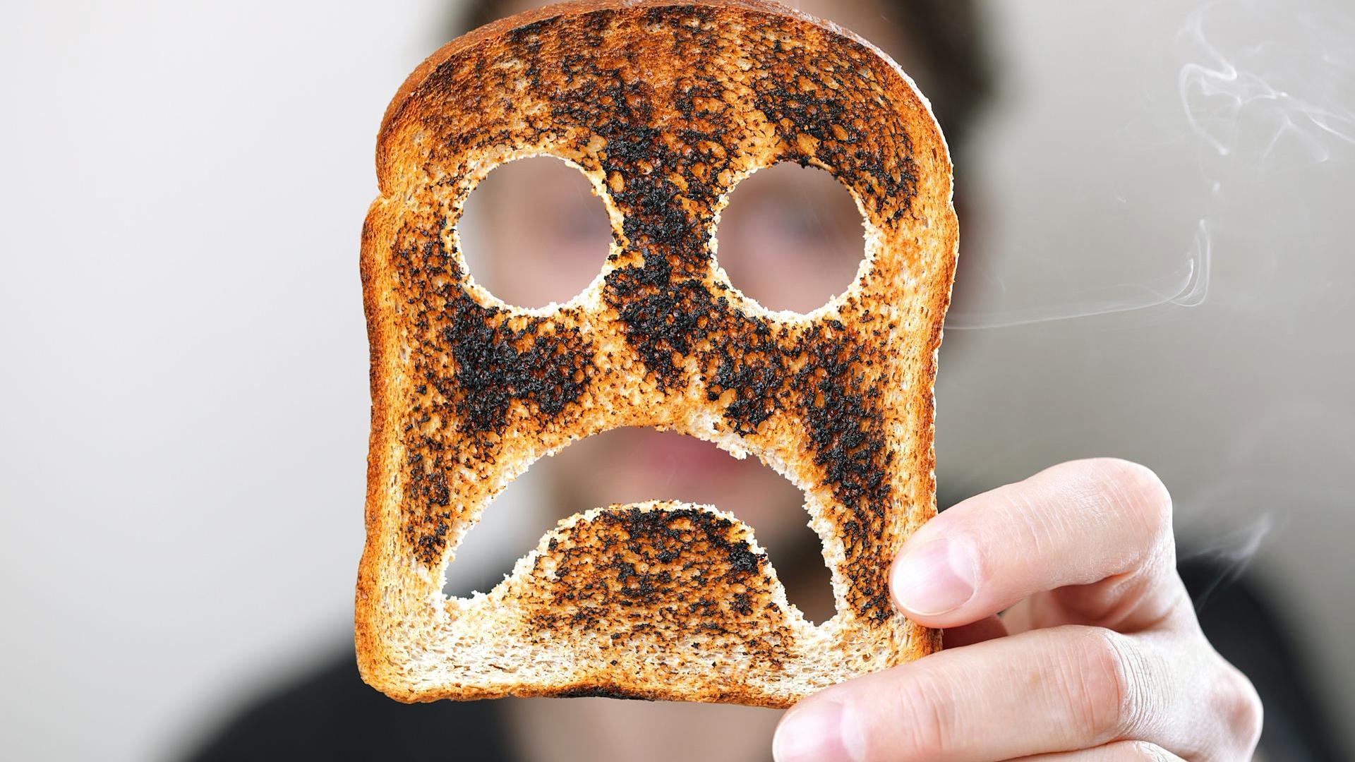 Una persona sujeta una tostada de pan de molde quemada con una cara triste./