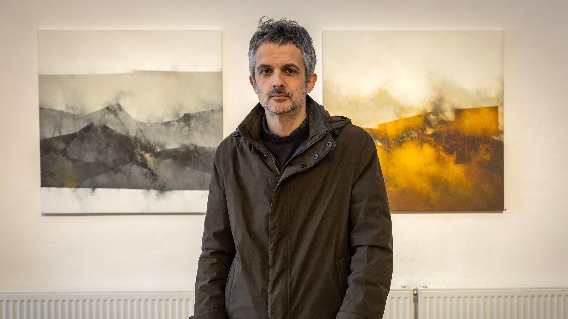 Javier Egiluz, posando junto a dos de sus obras en La Fábrica de Gomas. Los negros, grises y ocres son los colores protagonistas