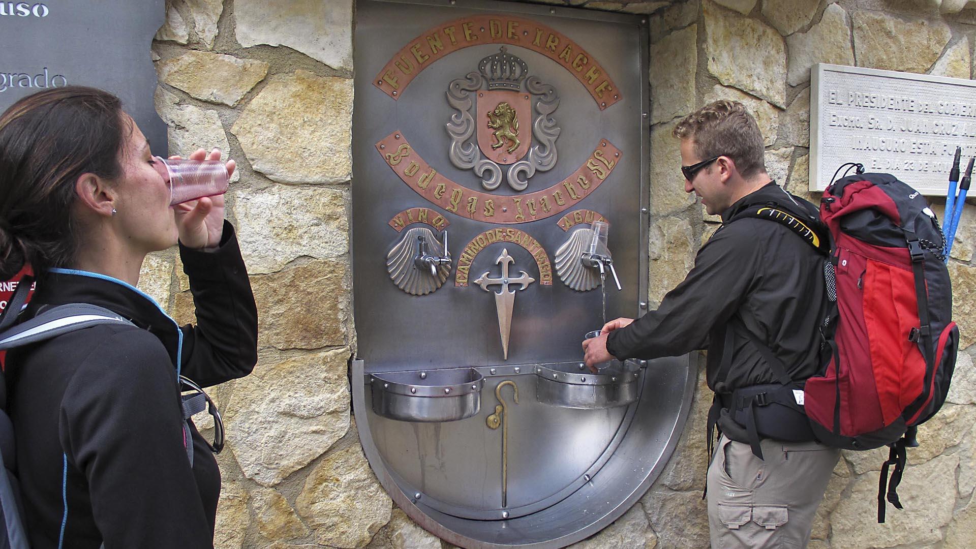 Dos peregrinos refrescan su trayecto del Camino de Santiago en la fuente de las Bodegas Irache