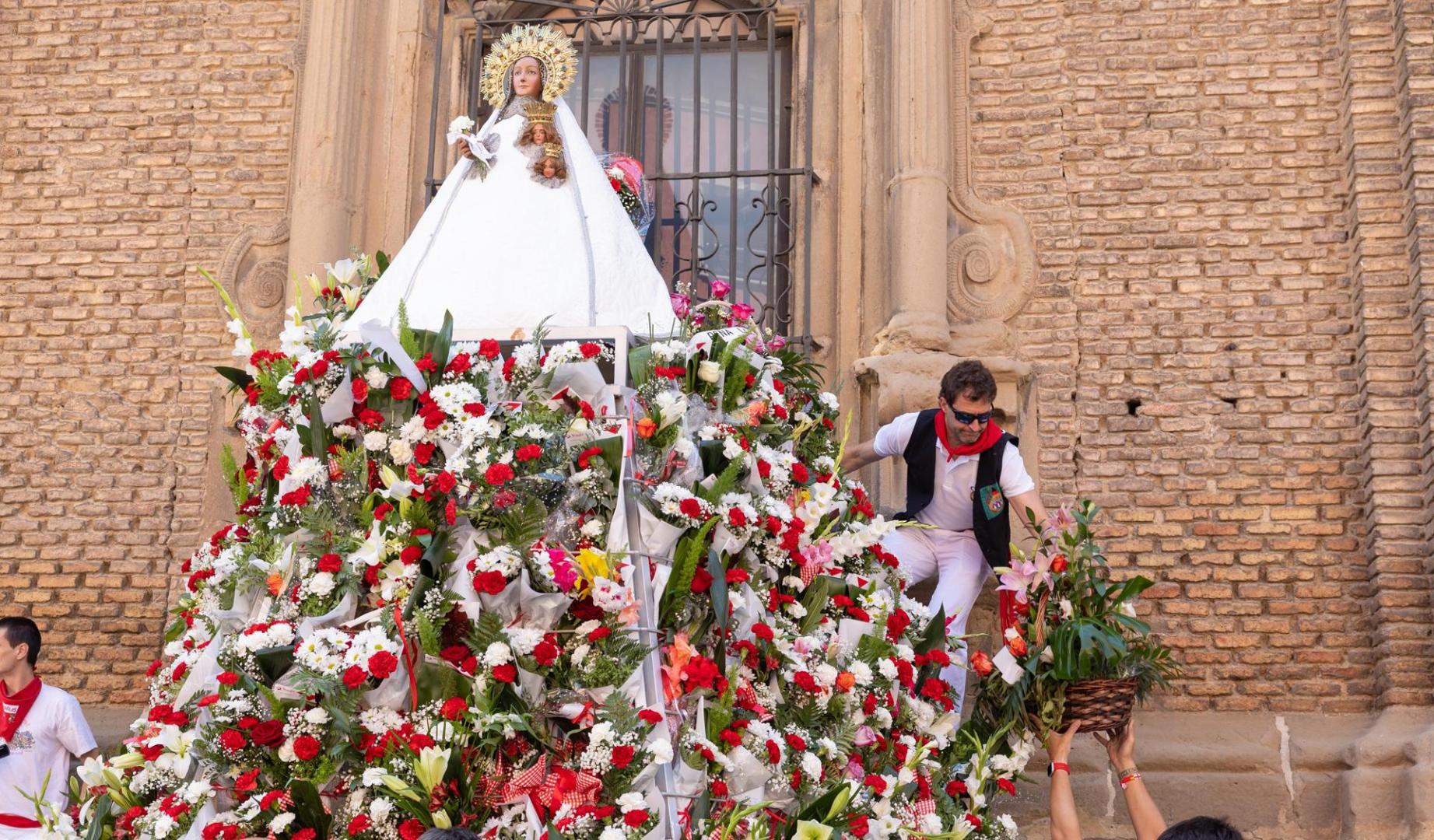 Cubierta de flores blancas y rojas, como el color de la fiesta. Así ha acabado Santa Ana tras la tradicional ofrenda floral realizada en el exterior de la Catedral de Santa María la Mayor de Tudela. Organizado por la peña La Teba, el acto ha reunido este mediodía a centenares de vecinos y miembros de la corporación municipal que se han acercado a dejar su ramo a la patrona de la localidad.