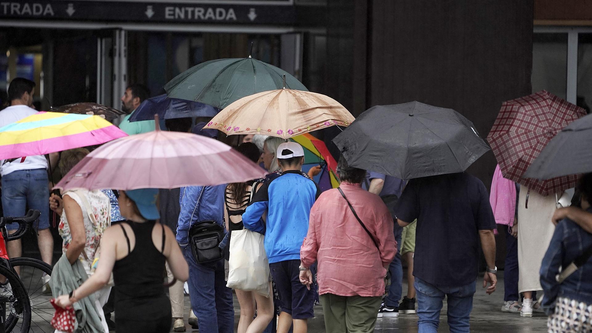 Varias personas despliegan paraguas en una calle de Gijón este mes de agosto