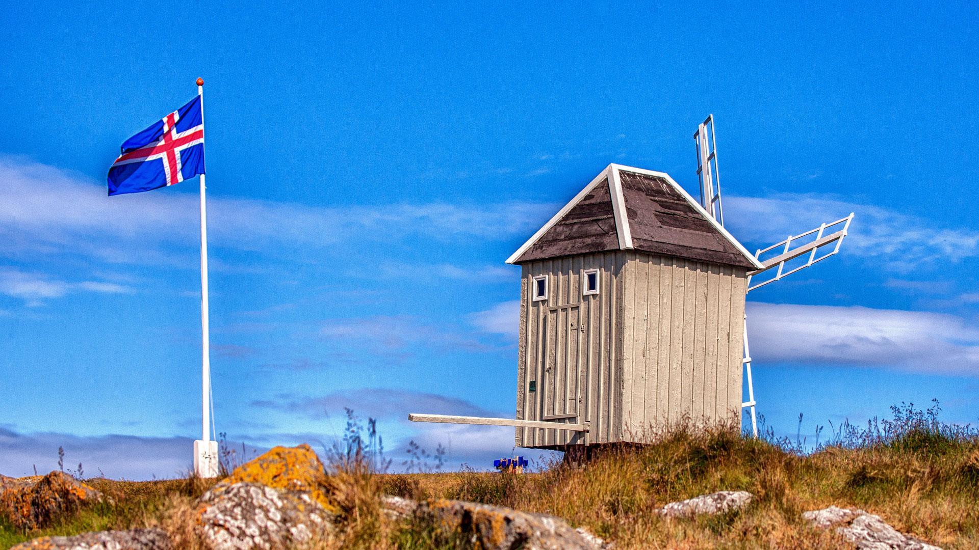 La bandera de Islandia ondea junto al único molino de viento antiguo  que queda en pie en el país, construido en 1840, en la isla de Vigur en la bahía de Isafjordur