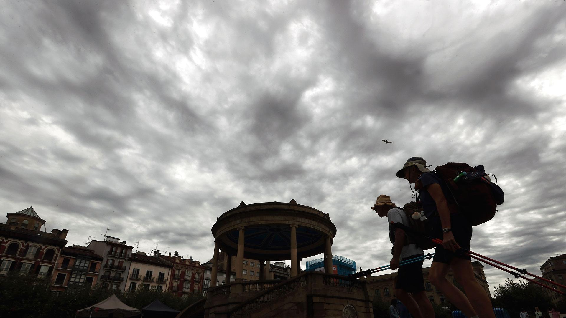 Dos turistas pasean por la Plaza del Castillo de Pamplona con un cielo tormentoso este jueves