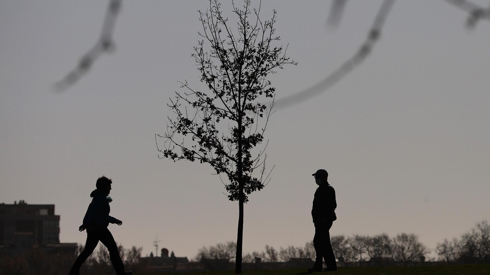 Un joven camina hacia el encuentro de una persona de más edad en una zona ajardinada