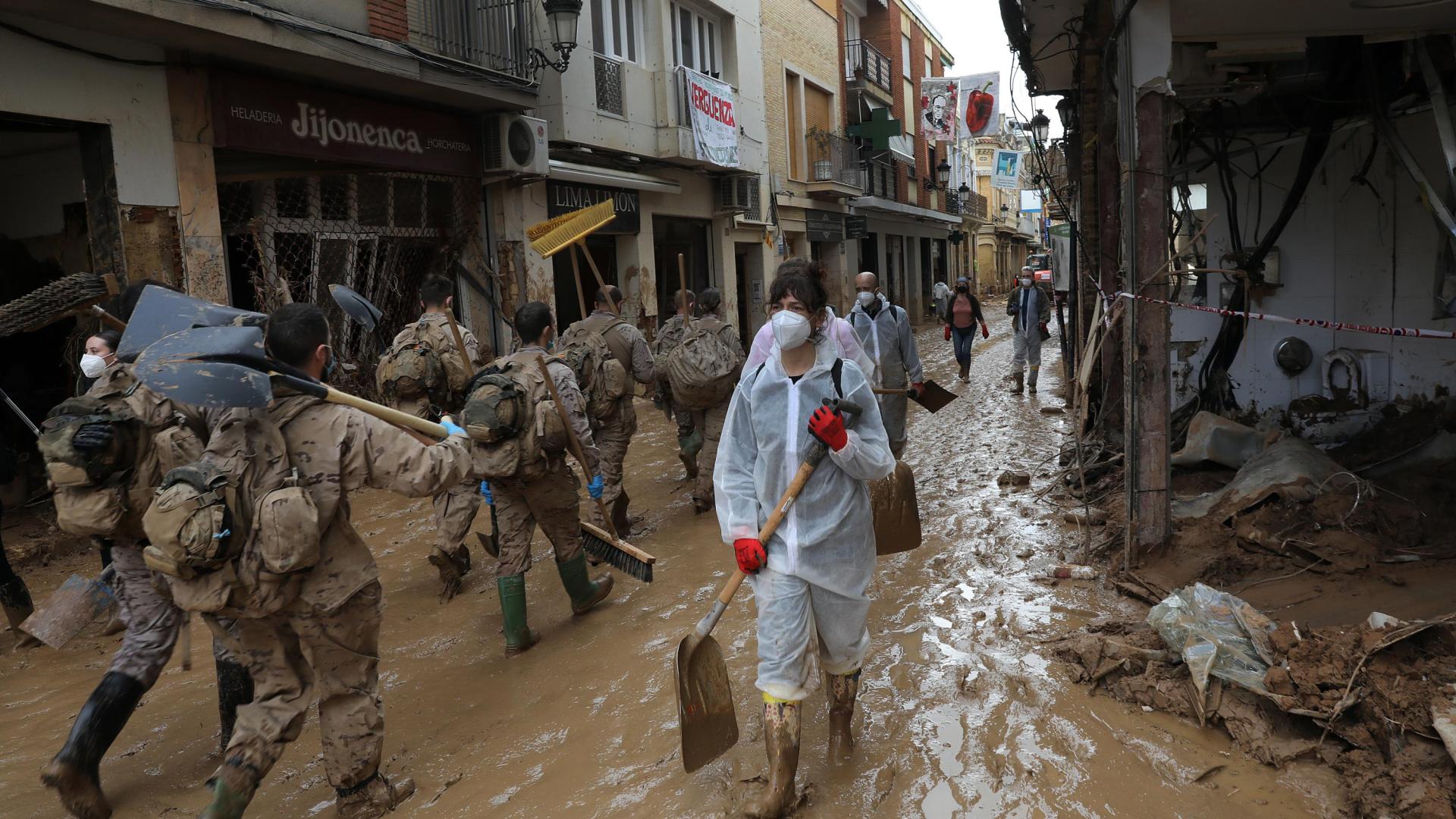 Un grupo de voluntarios pala en mano se cruza con efectivos del ejército en una de las calles de Paiporta, aún anegadas de barro.