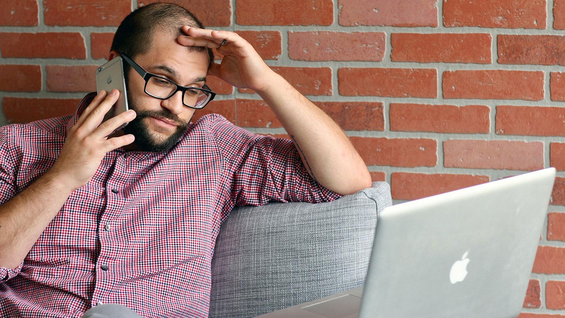 Un hombre estresado consulta su ordenador mientras habla por el móvil