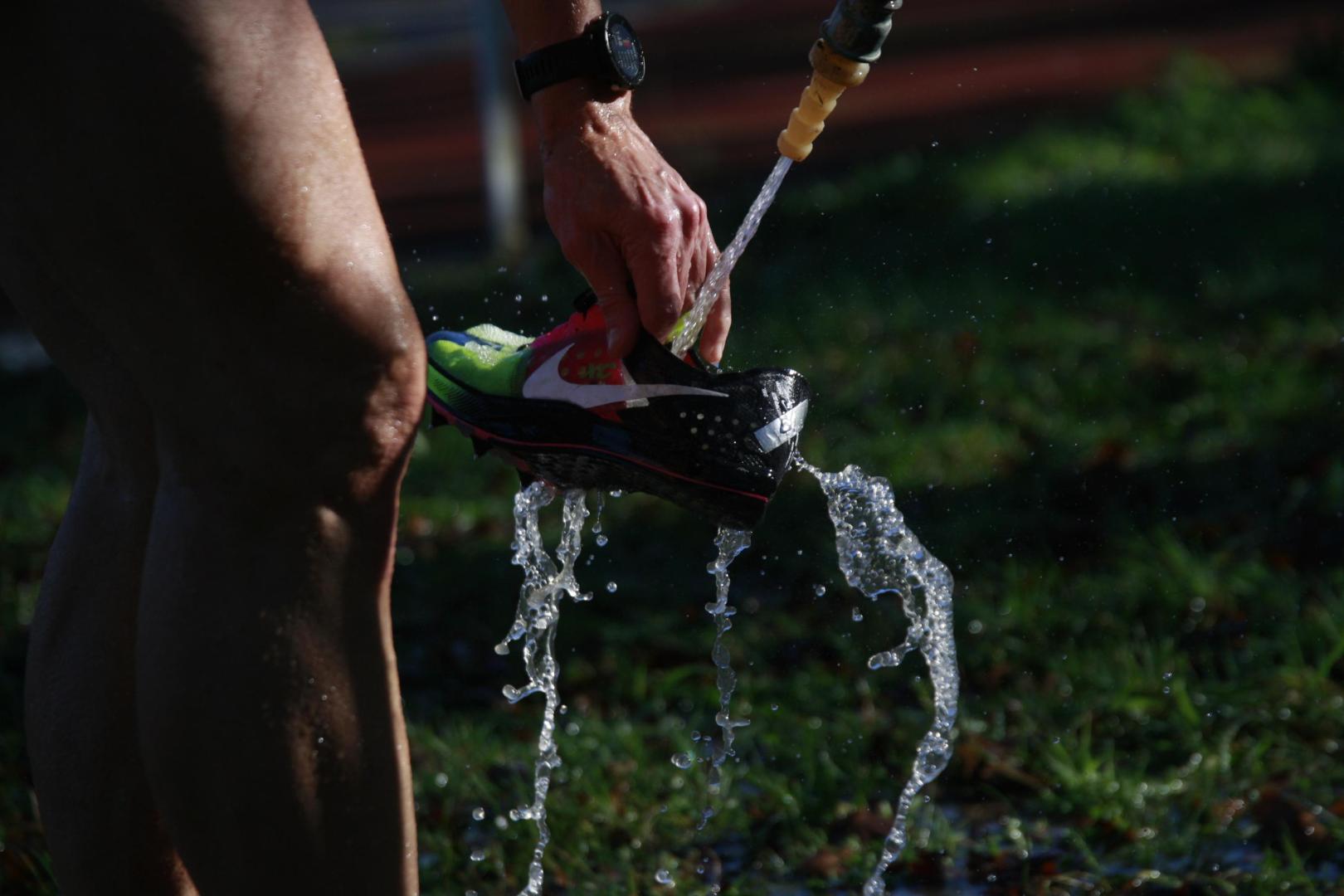 Un atleta, lavando del barro su zapatilla con una manguera tras la carrera.