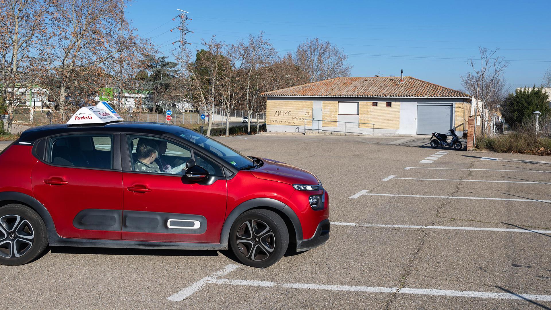 Un coche de autoescuela, con el aula de exámenes, al fondo /