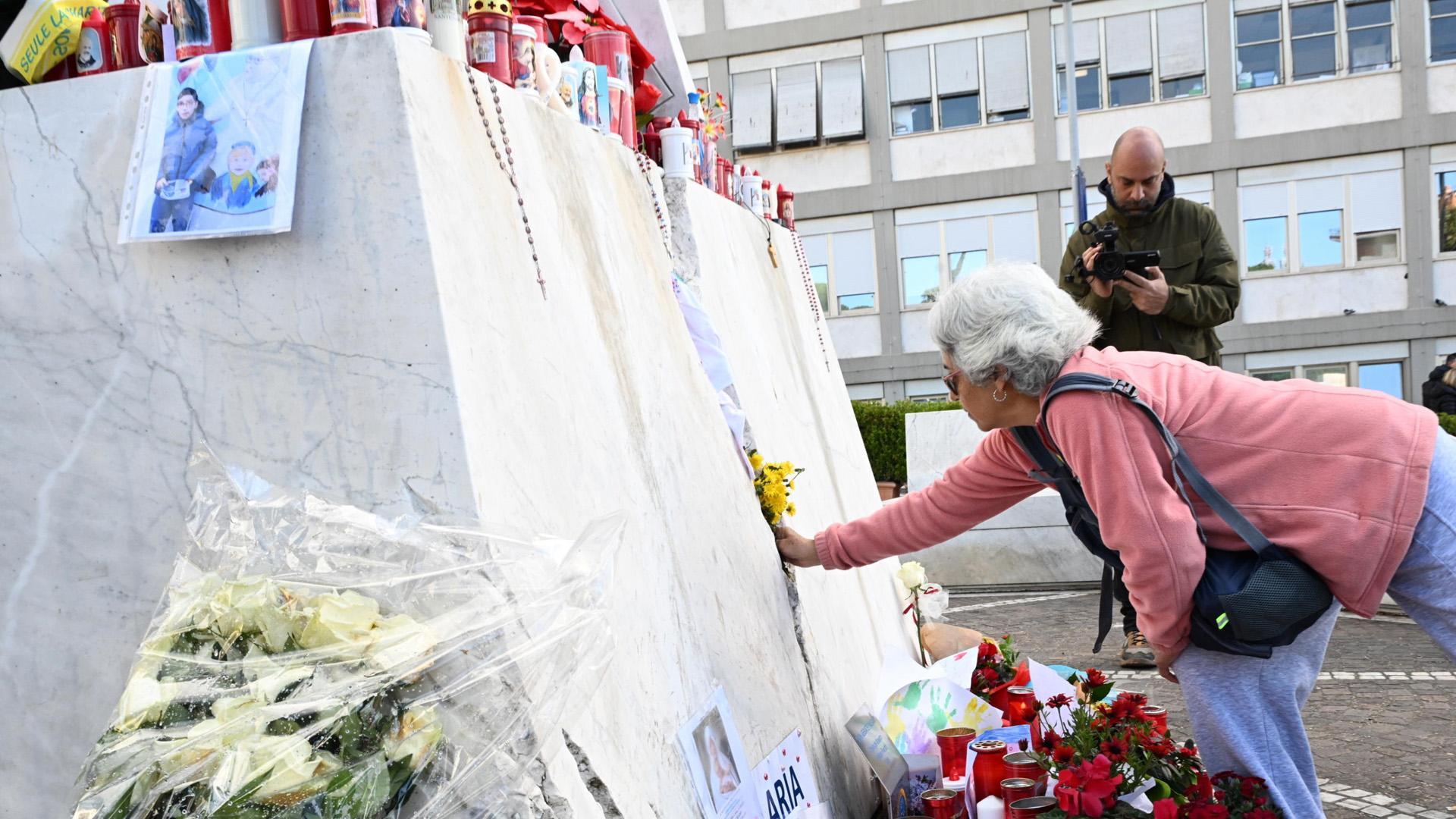 Una mujer deposita flores a los pies de la estatua de Juan Pablo II, en el exterior del hospital Gemelli, donde continúa ingresado el papa Francisco