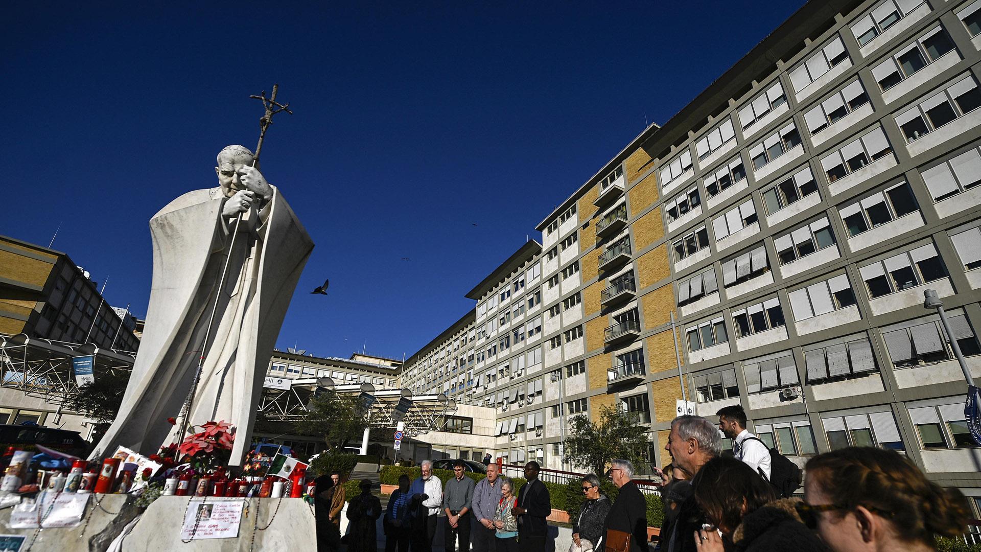 Fieles rezan junto a la estatua de Juan Pablo II, en el exterior del hospital Gemelli