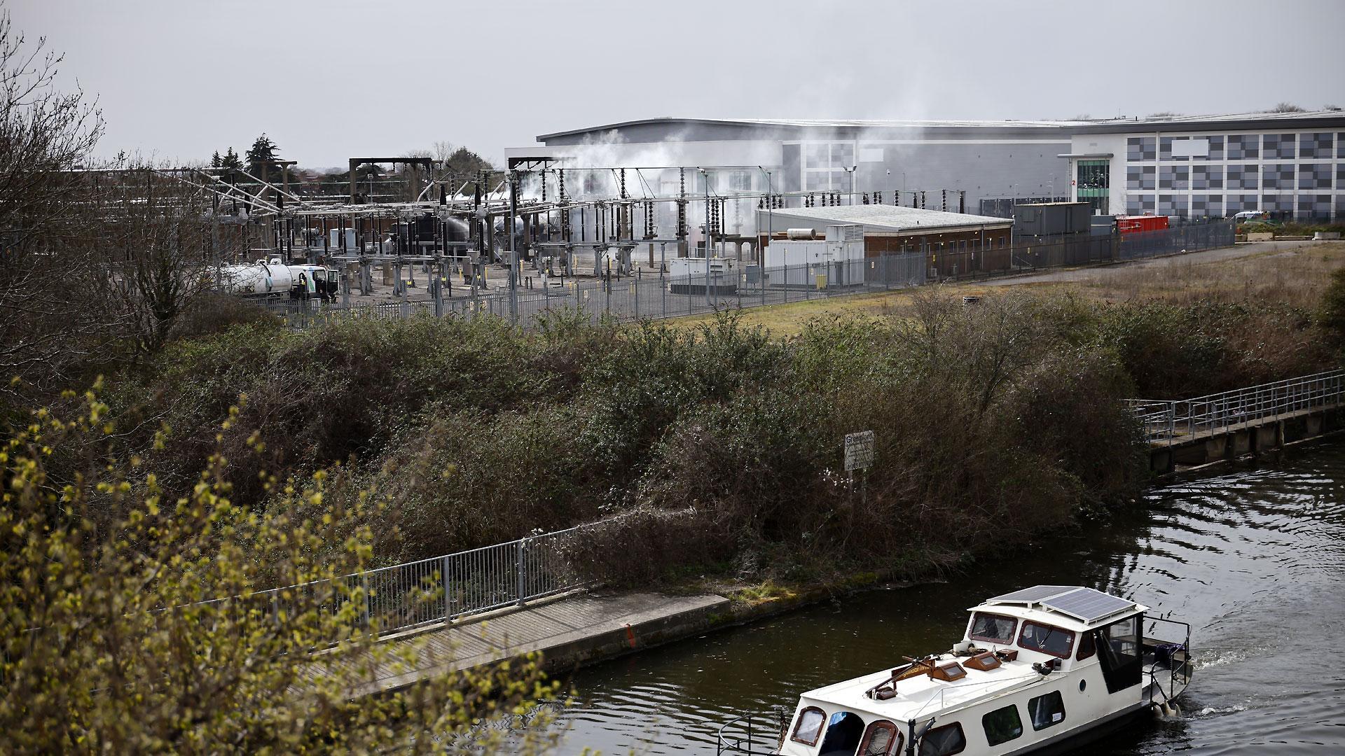 Un bote pasa por el canal situado junto a la subestación eléctrica de la localidad británica de Hayes que ha sufrido un incendio y ha obligado a cerrar el aeropuerto de Heathrow durante un día