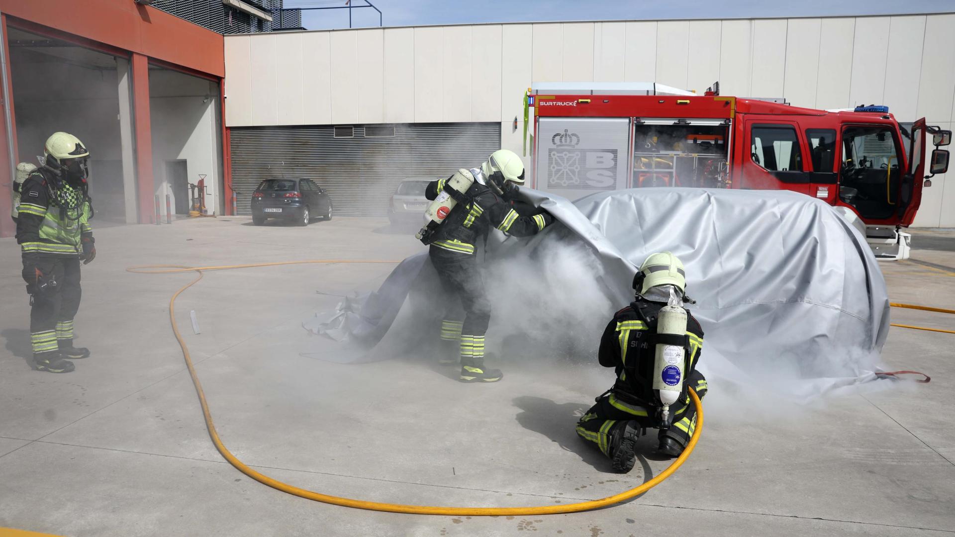 Efectivos de bomberos del parque de Trinitarios realizan una demostración con la manta térmica para sofocar el incendio de baterías en un vehículo