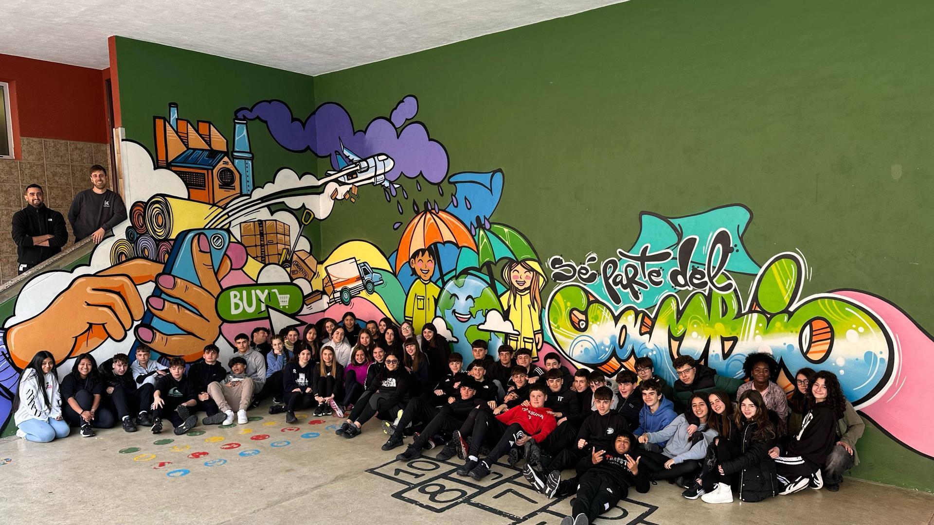 El alumnado de 3º de la ESO con el mural pintado en un rincón del patio con el que invita a reflexionar sobre las compras