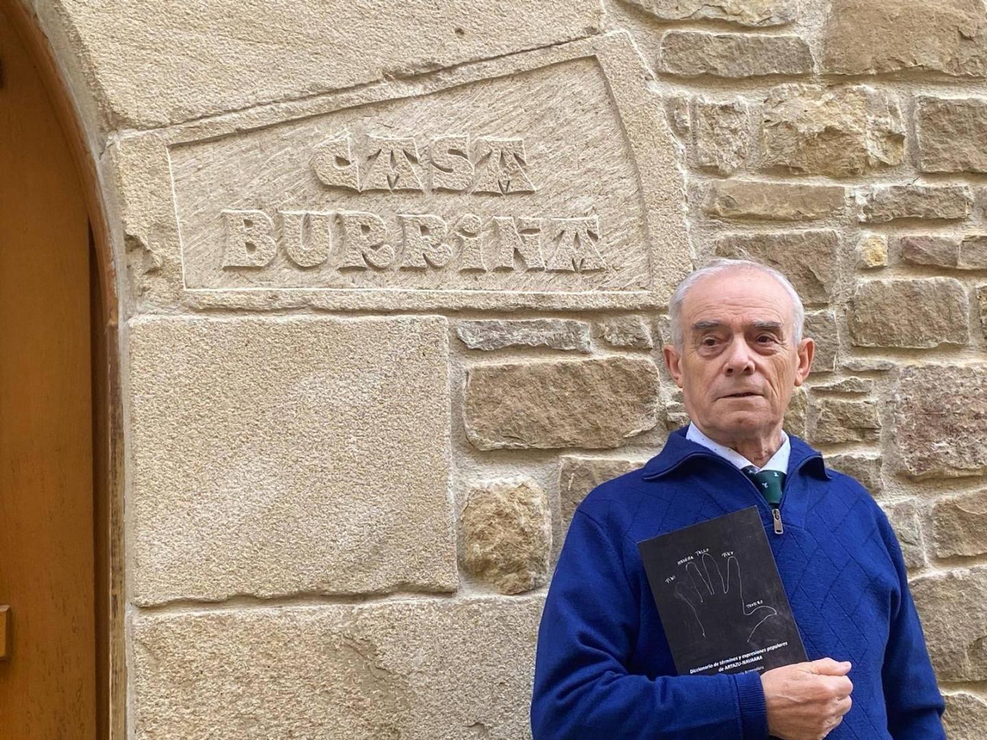 Jesús Alegría en la puerta de su casa natal de Artazu con un ejemplar de su diccionario en las manos