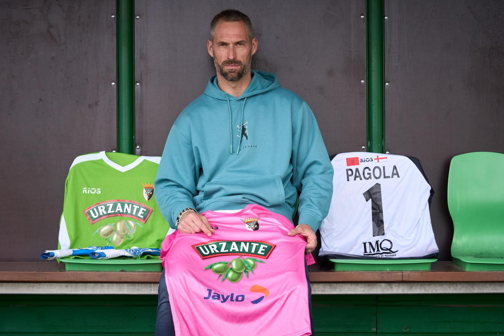Con tres camisetas del Tudelano, Mikel Pagola posa en la marquesina que tiene como banquillo el campo de Peritos de Villava.