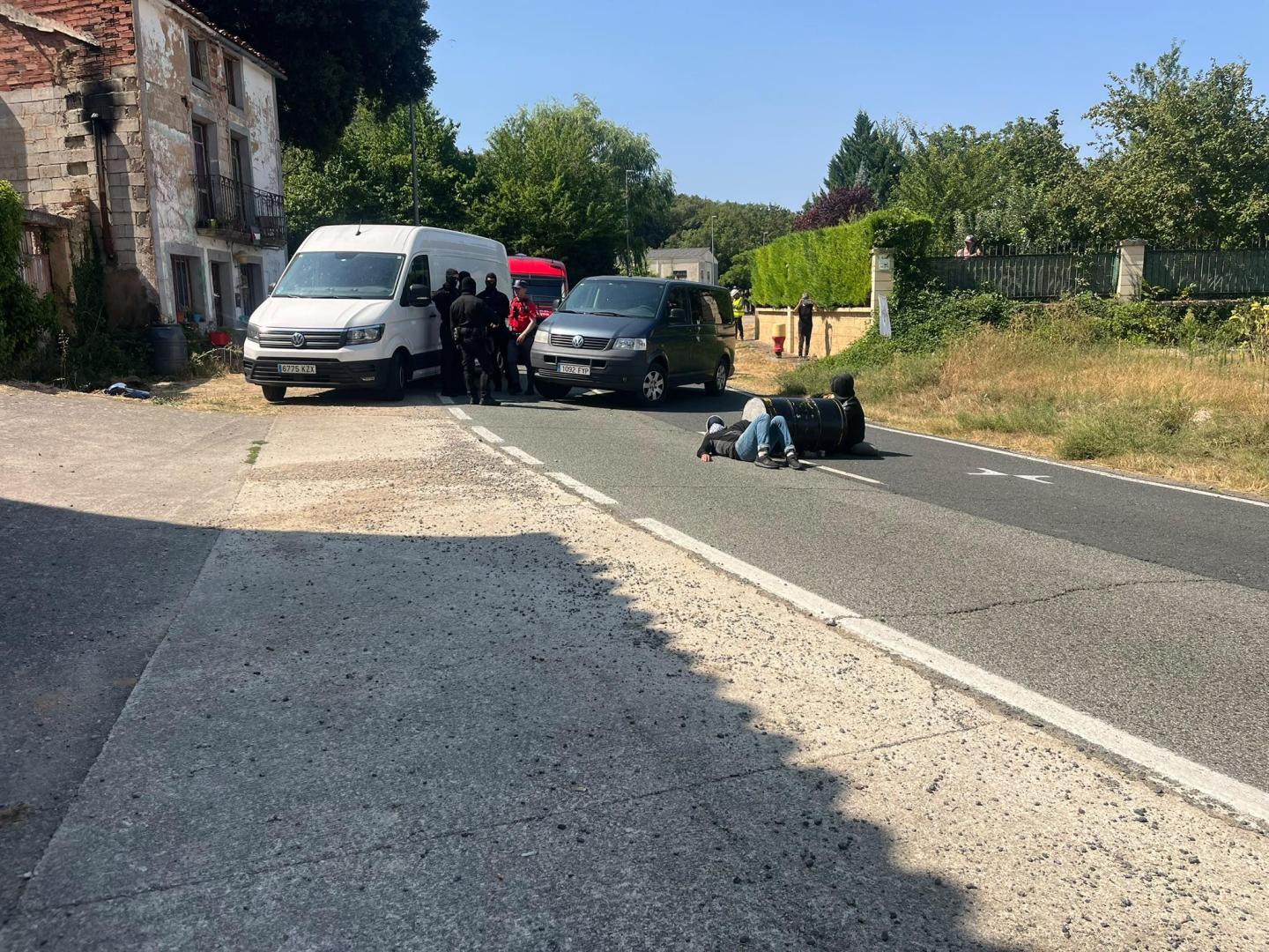 Los dos manifestantes en medio de la calzada atados al barril y agentes de la Policía Foral al fondo de la imagen