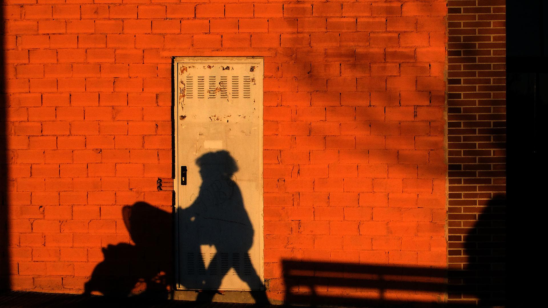 Una mujer empuja una silleta de bebé y su sombra se proyecta en la fachada de la pared de una bajera